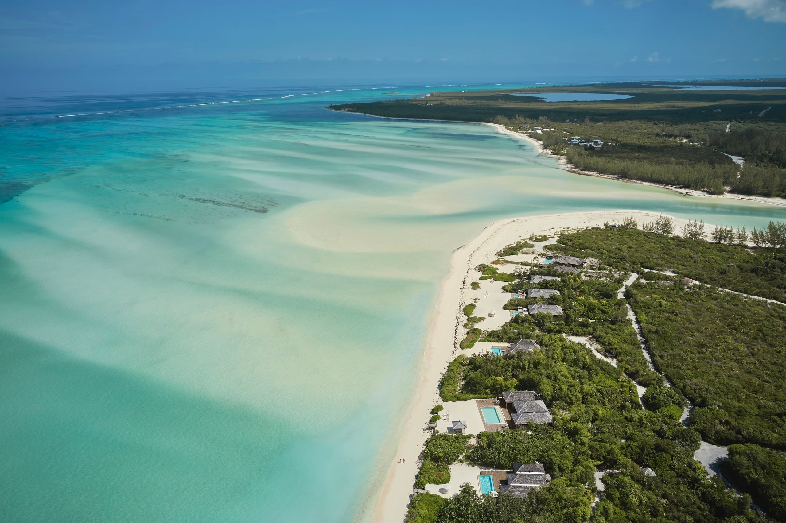 COMO Parrot Cay, Turks and Caicos — Aerial view of beachfront luxury villas nestled in tropical vegetation along turquoise lagoon and white sand beach.