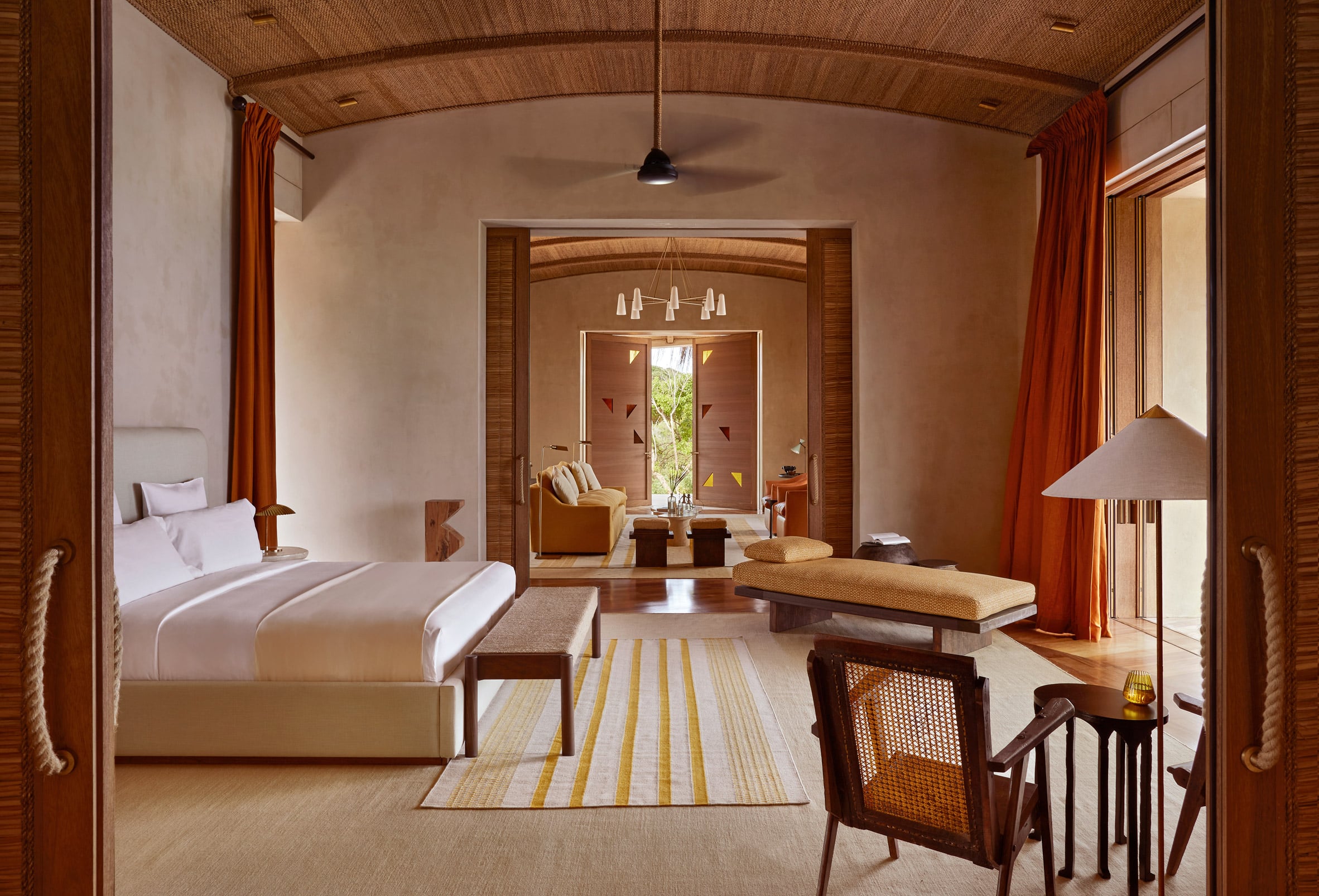 Kisawa Sanctuary, Africa — Minimalist villa bedroom with teak wood ceiling, curved archways, terracotta walls, and open-air lounge overlooking tropical gardens through floor-to-ceiling doors.