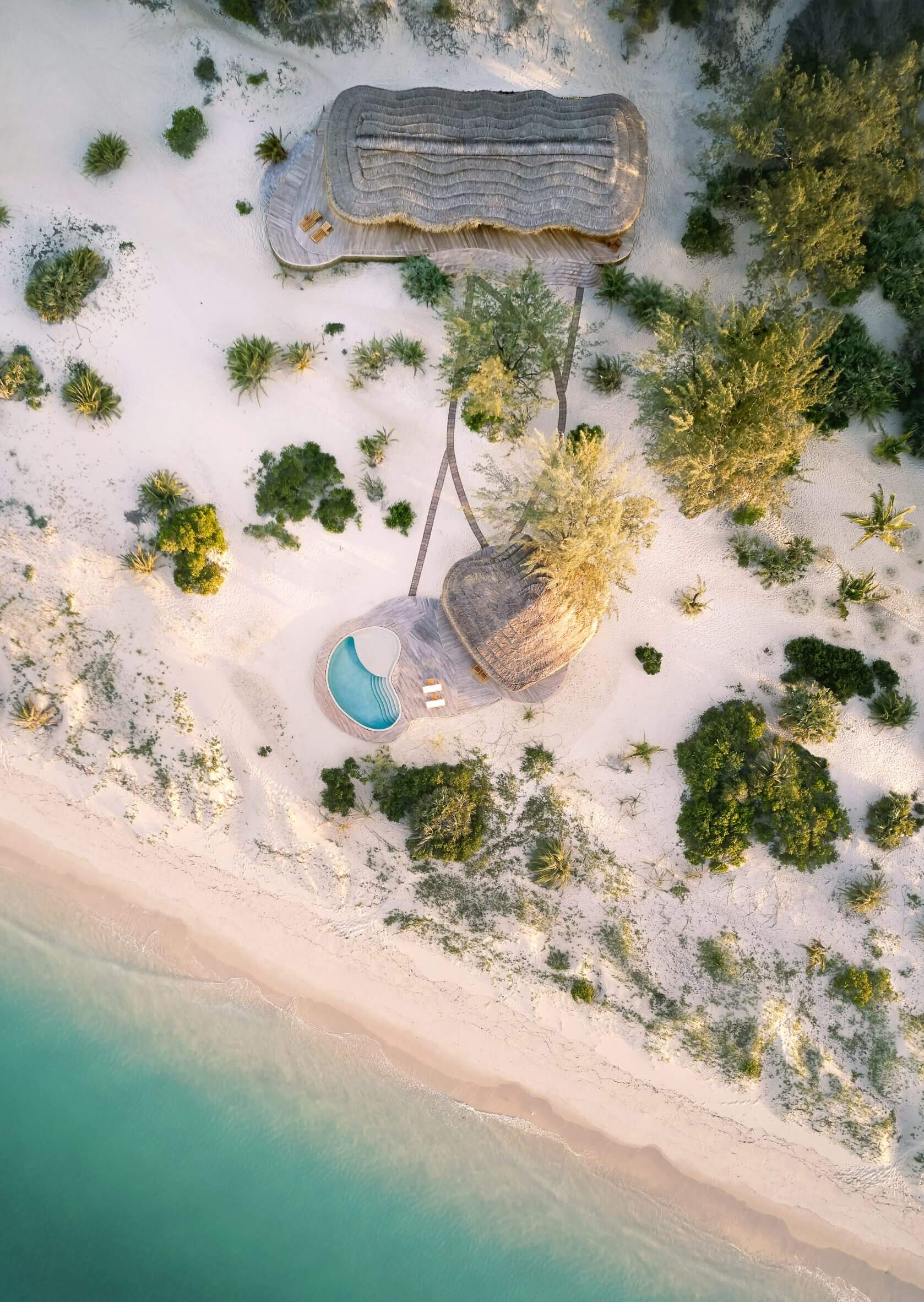 Kisawa Sanctuary, Africa — Aerial view of curved boardwalk and kidney-shaped pool nestled in white sand surrounded by sparse vegetation and turquoise ocean waters.