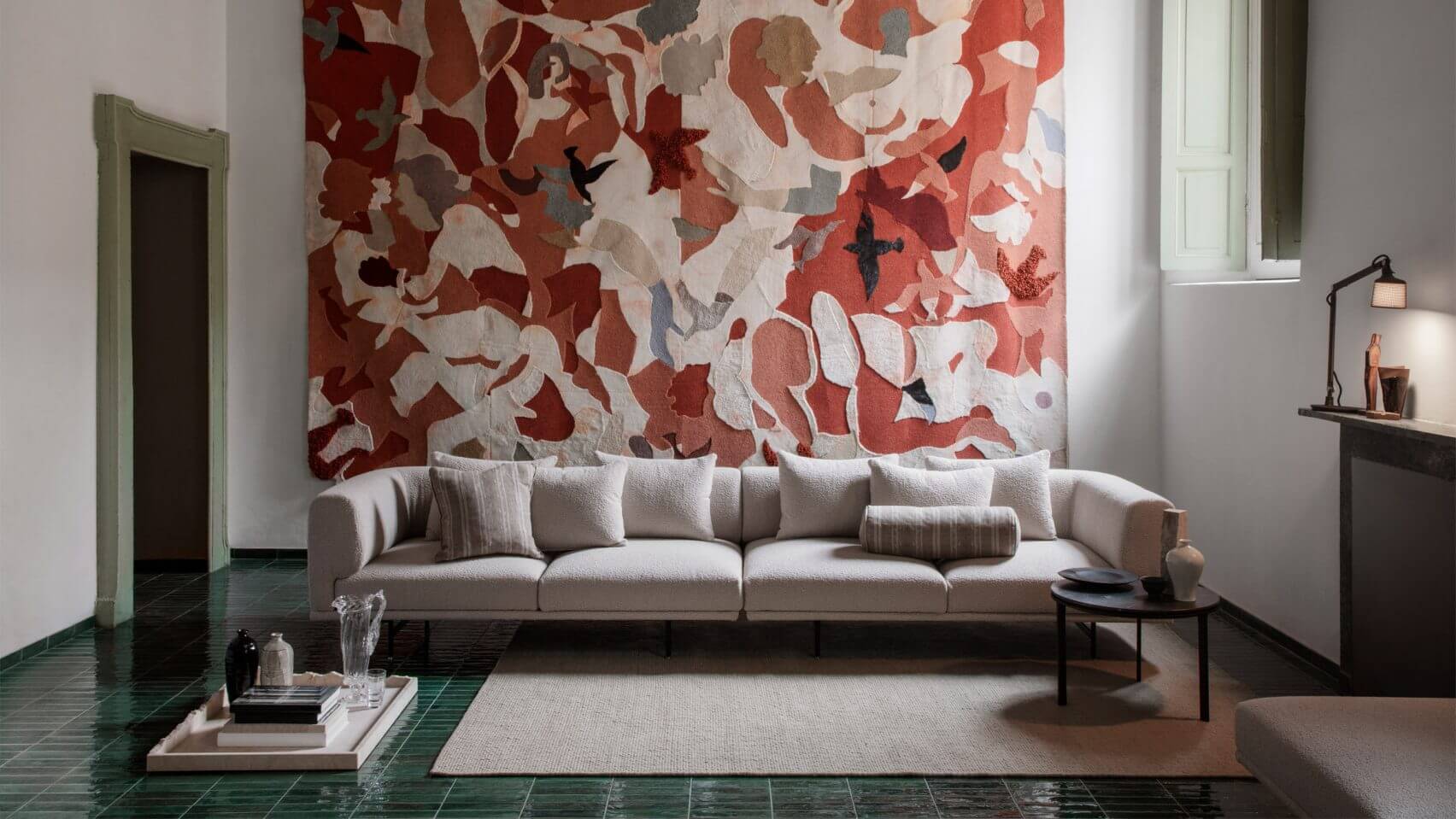Vipp Palazzo Monti, Italy — Minimalist living room with cream modular sofa, red botanical wall tapestry, green tile flooring, and contemporary furnishings in luxury Italian hotel interior design.