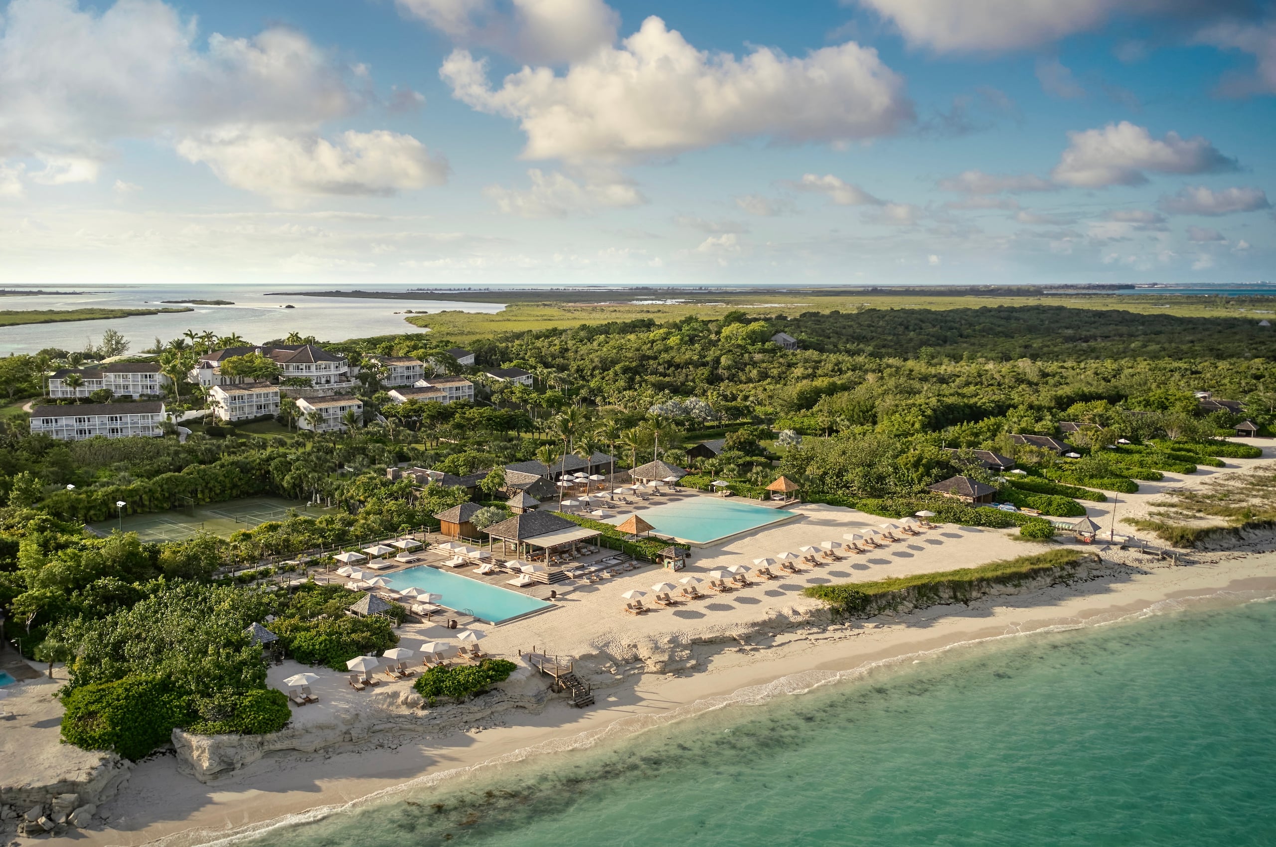 COMO Parrot Cay, North America — Beachfront luxury resort with dual pools, lounge chairs, and mangrove-bordered sand overlooking turquoise waters and verdant islands.