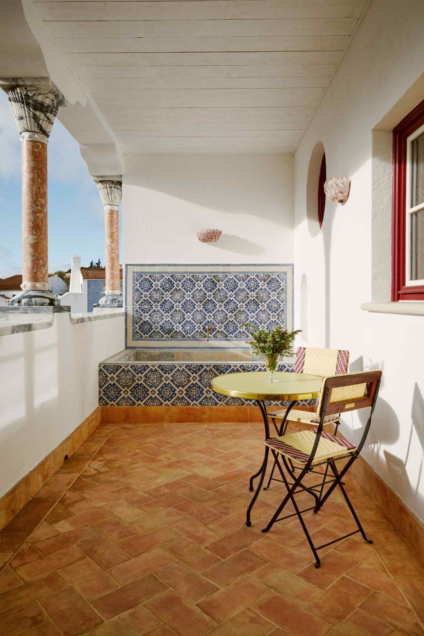 Vermelho, Europe — Covered terrace with decorative blue-and-white tilework, ornate columns, terracotta herringbone flooring, and vintage bistro seating overlooking coastal landscape.