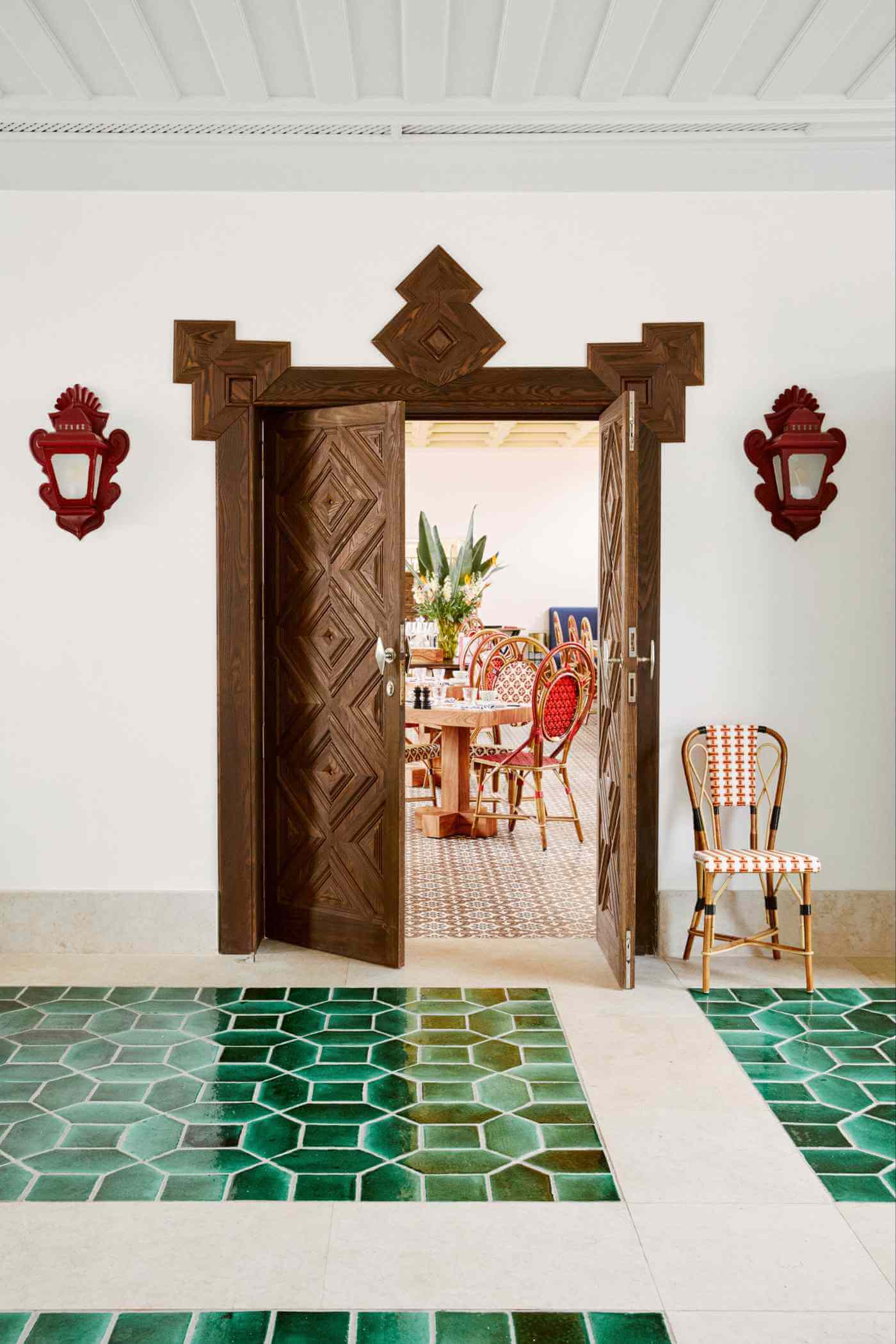 Xtian Restaurant, Europe — Ornate wooden double doors with geometric inlay opening to dining room, flanked by red wall sconces and green hexagonal tile floor.