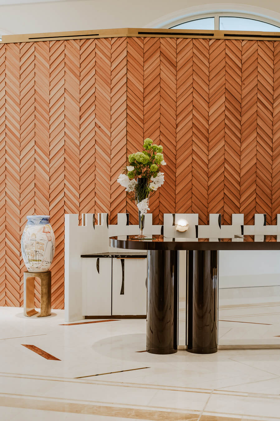 Carlton Cannes, Cannes, France — Herringbone brick wall with white geometric shelving, polished black cylindrical pedestals, white floral arrangement, and minimalist interior design.