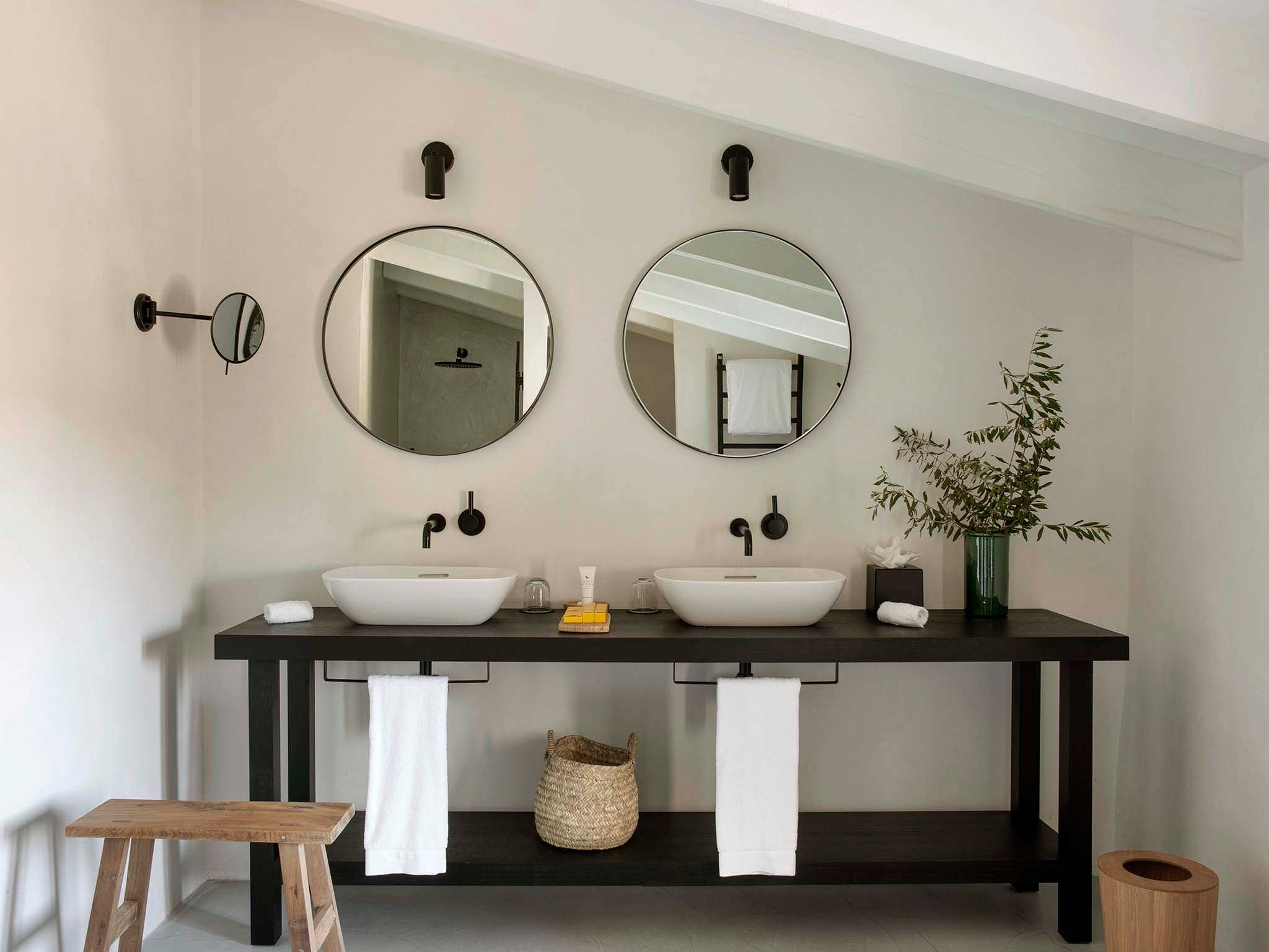 Finca Serena, Balearic Islands — Minimalist bathroom vanity with dual white vessel sinks, black metal fixtures, circular mirrors, and natural materials under soft light.