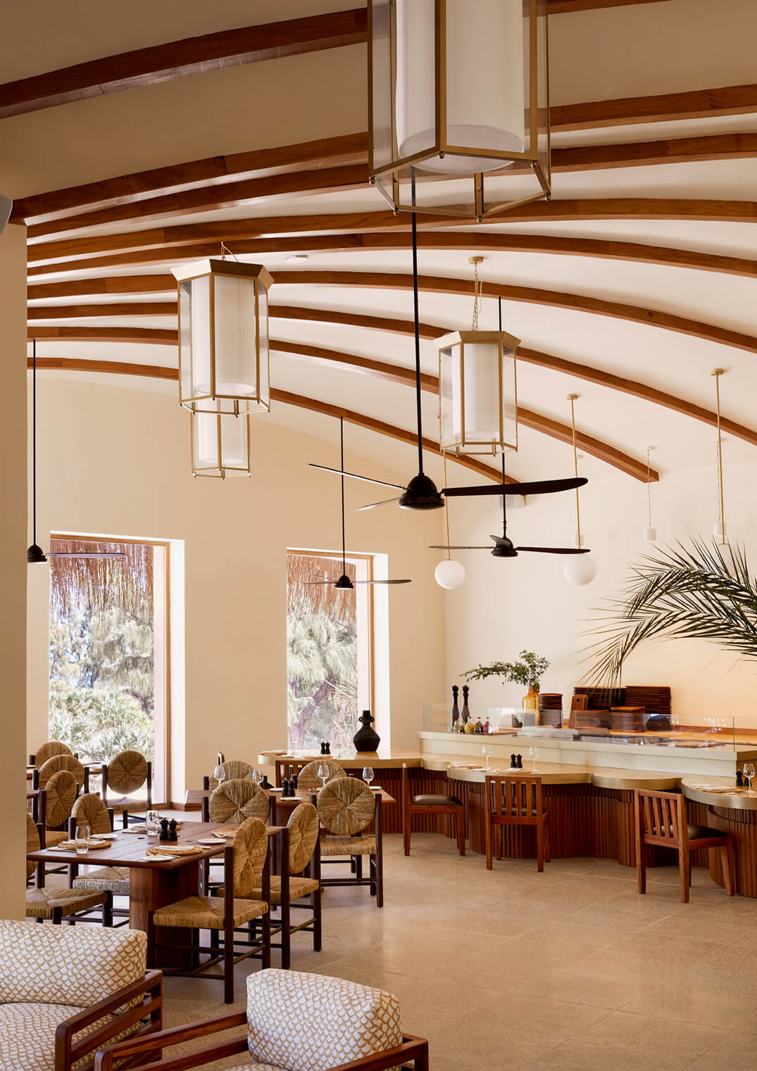 The Main Terrace & The Lobby — Main Terrace & Lobby, Africa — Soaring timber-beamed dining space with curved wooden ceiling, pendant lights, natural daylight, woven-back chairs, and minimalist bar counter.