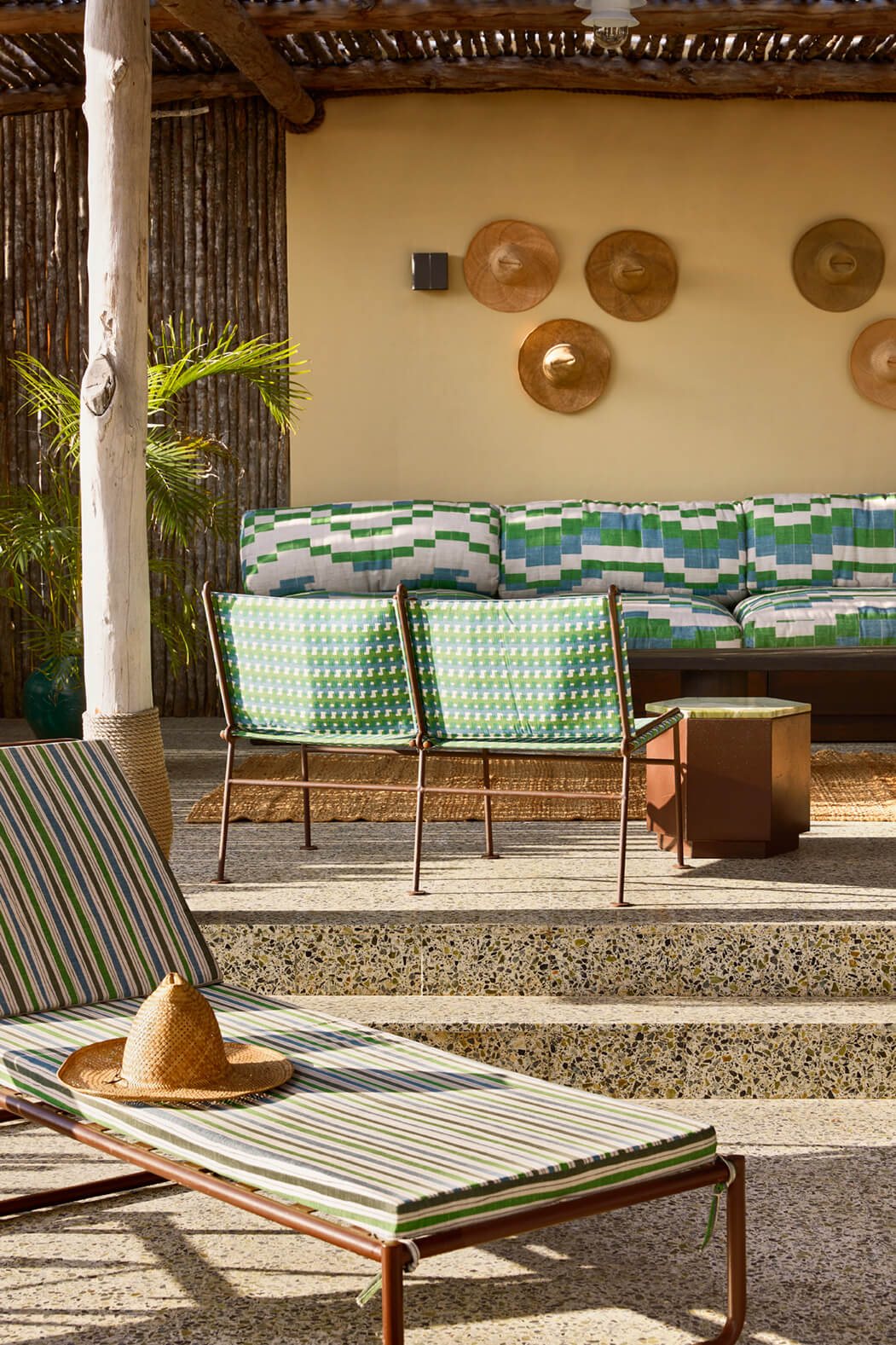 Cove Mussassa, Africa — Covered patio with striped lounge chairs, woven hats, wooden side tables, and cream walls decorated with woven plates under timber pergola.