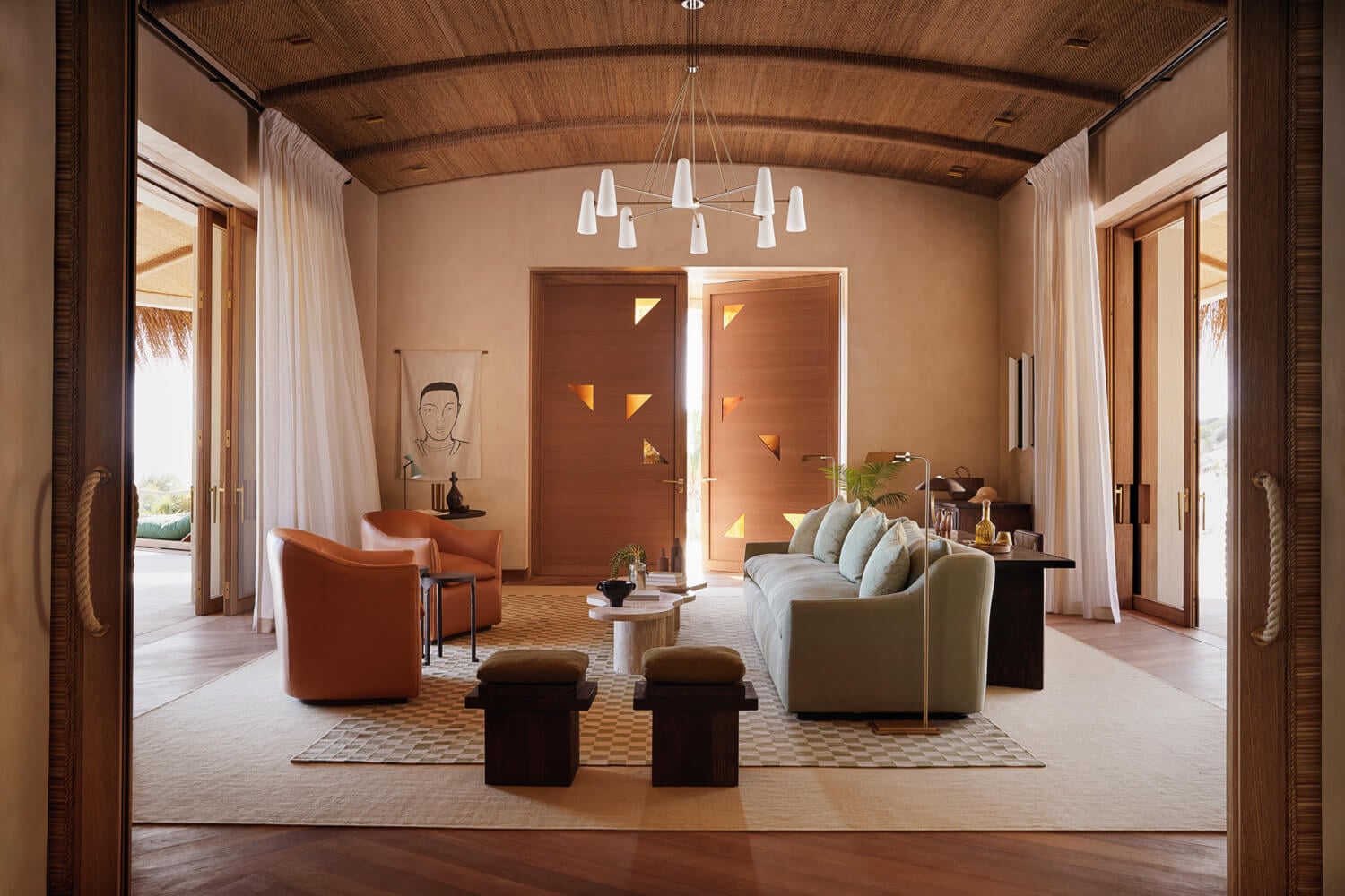 Kisawa Sanctuary, Africa — Warm-toned living room with curved ceiling, pendant chandelier, cream sofa, terracotta chairs, geometric rugs, and floor-to-ceiling glass doors opening to landscape.