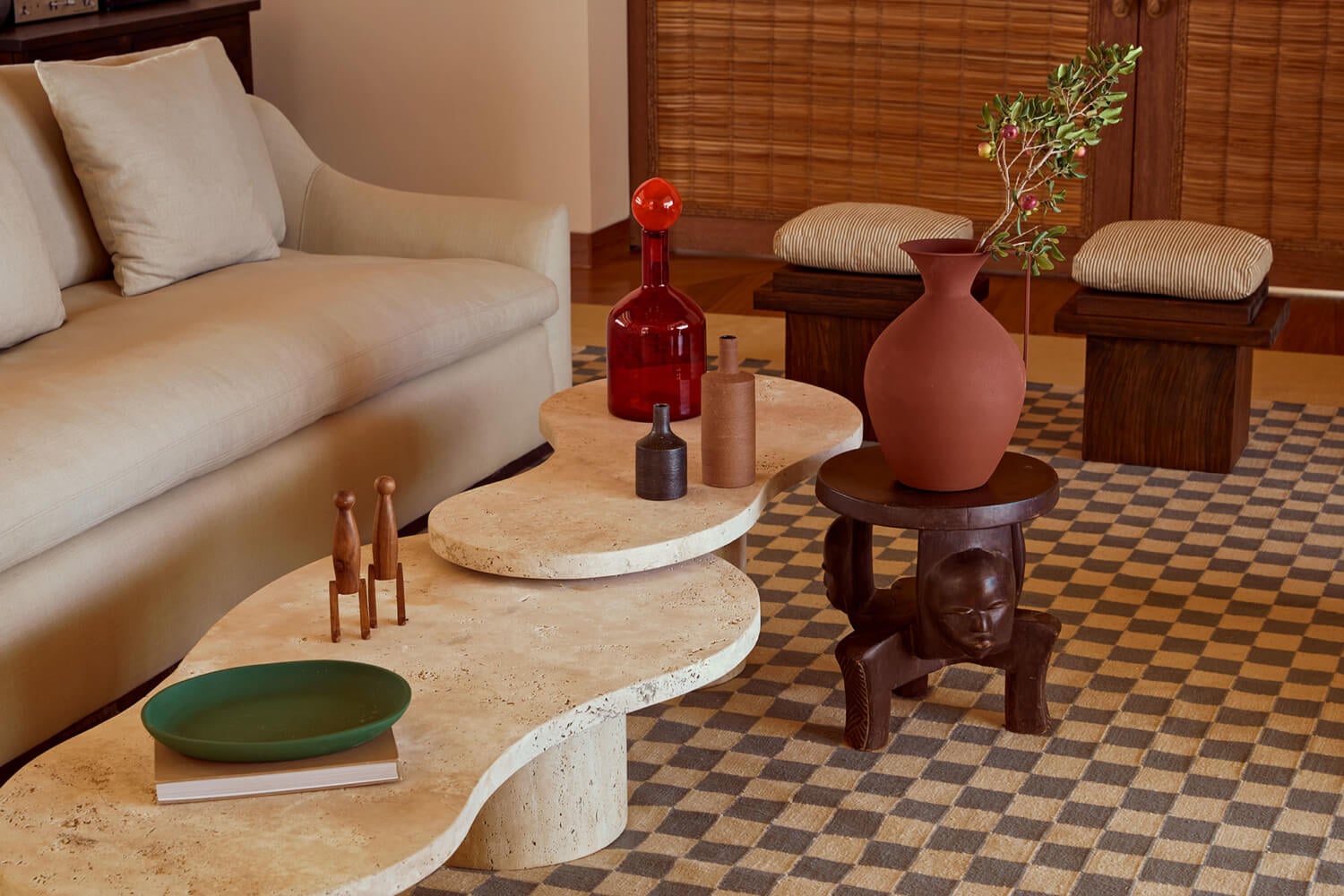Kisawa Sanctuary, Africa — Travertine side tables with sculptural wooden stool, terracotta vessel, and minimalist décor in warm-toned lounge with checkered tile flooring.