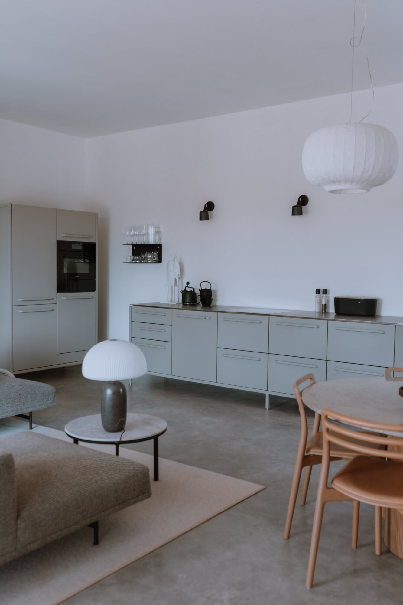 Villa Quercia, Italy — Minimalist open-plan kitchen and dining space with light cabinetry, concrete flooring, pendant lighting, and natural wood chairs under soft daylight.