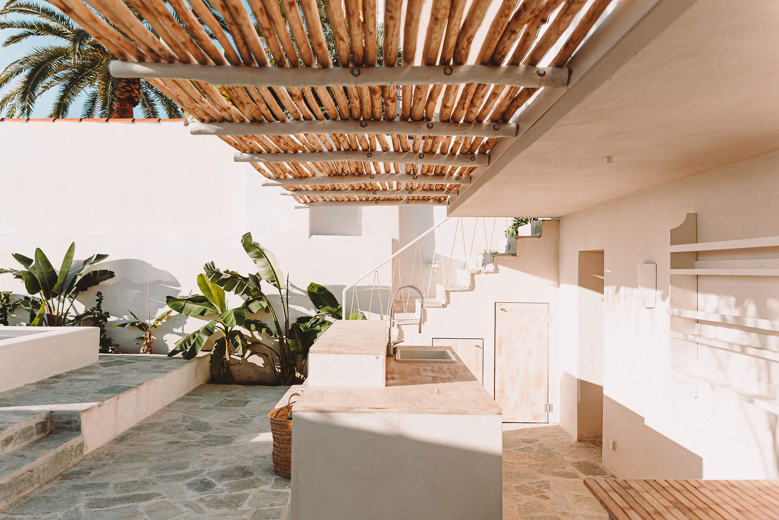 Casa Santa Teresa, Europe — Minimalist villa terrace with wooden pergola, white stone architecture, potted palms, and geometric shadows cast through latticed ceiling.