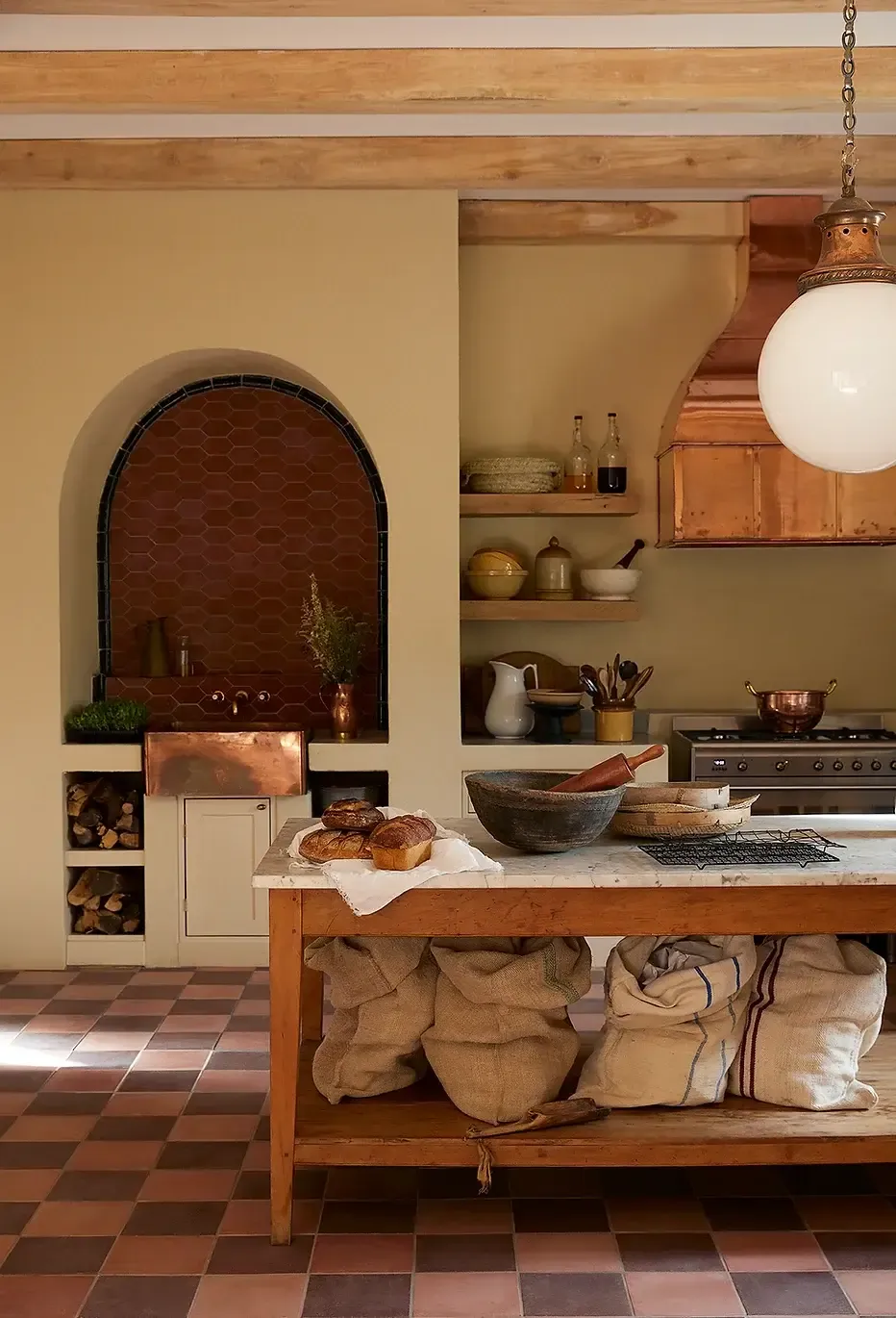 Sterrekopje, Africa — Warm-toned kitchen with arched brick fireplace, wooden island, open shelving, terracotta tile floor, and pendant lighting.