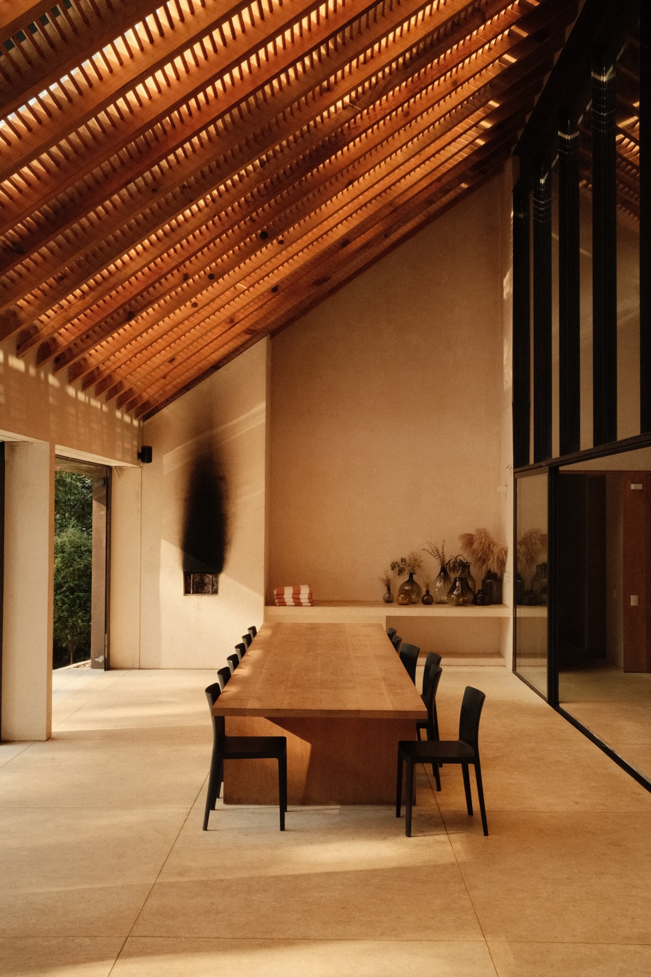 Casa Zarzales, Mexico — Minimalist dining room with wooden table, black chairs, terracotta walls, and dramatic timber ceiling with slated louvers casting striped light.