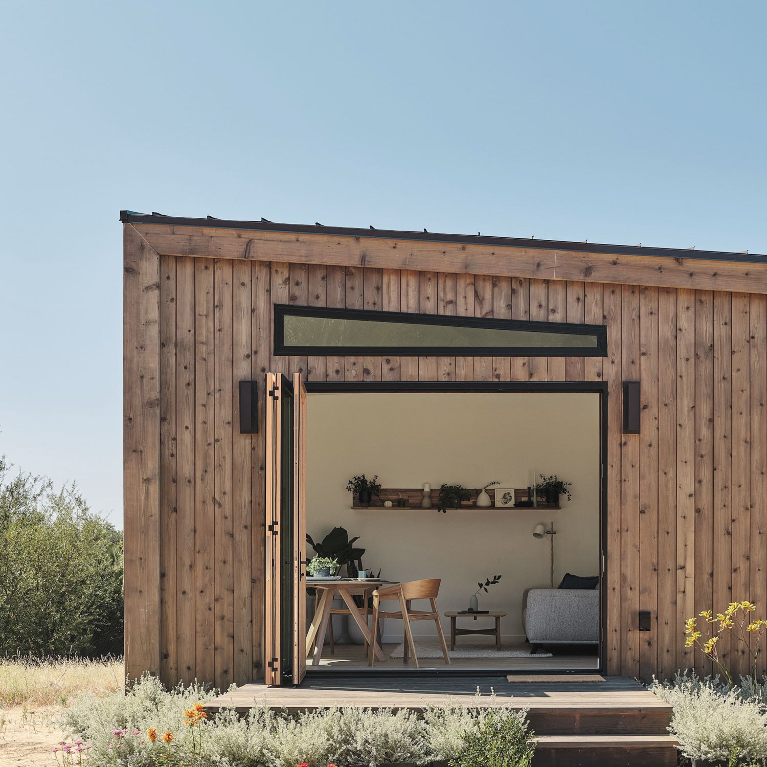 Abodu x Koto, North America — Modern wooden prefab cabin with charred timber exterior, minimalist interior visible through large glass doors, desert landscape setting.