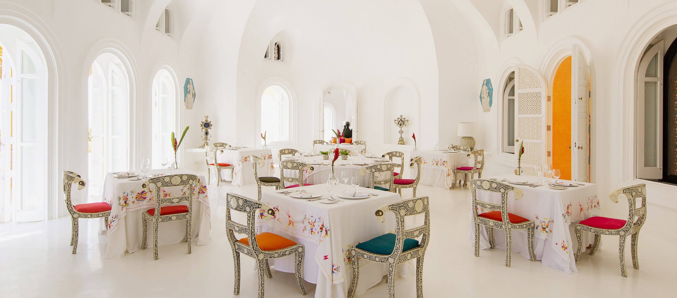 La Loma, Mexico — Luminous dining room with arched ceilings, ornate chairs with jewel-toned seats, white tablecloths, and abundant natural light from arched windows.