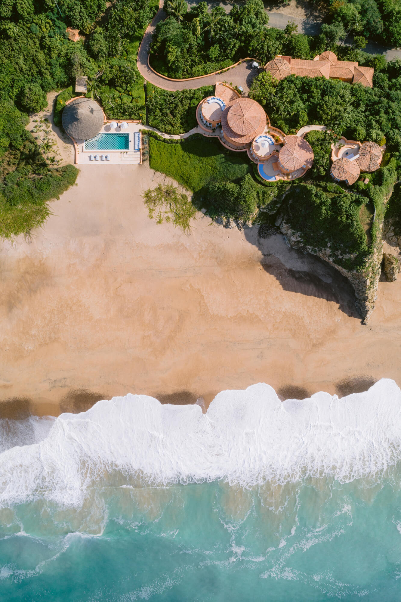 Playa Cuixmala, Mexico — Aerial view of beachfront luxury resort with distinctive domed structures, infinity pool, and lush tropical forest overlooking turquoise waves and white sand.