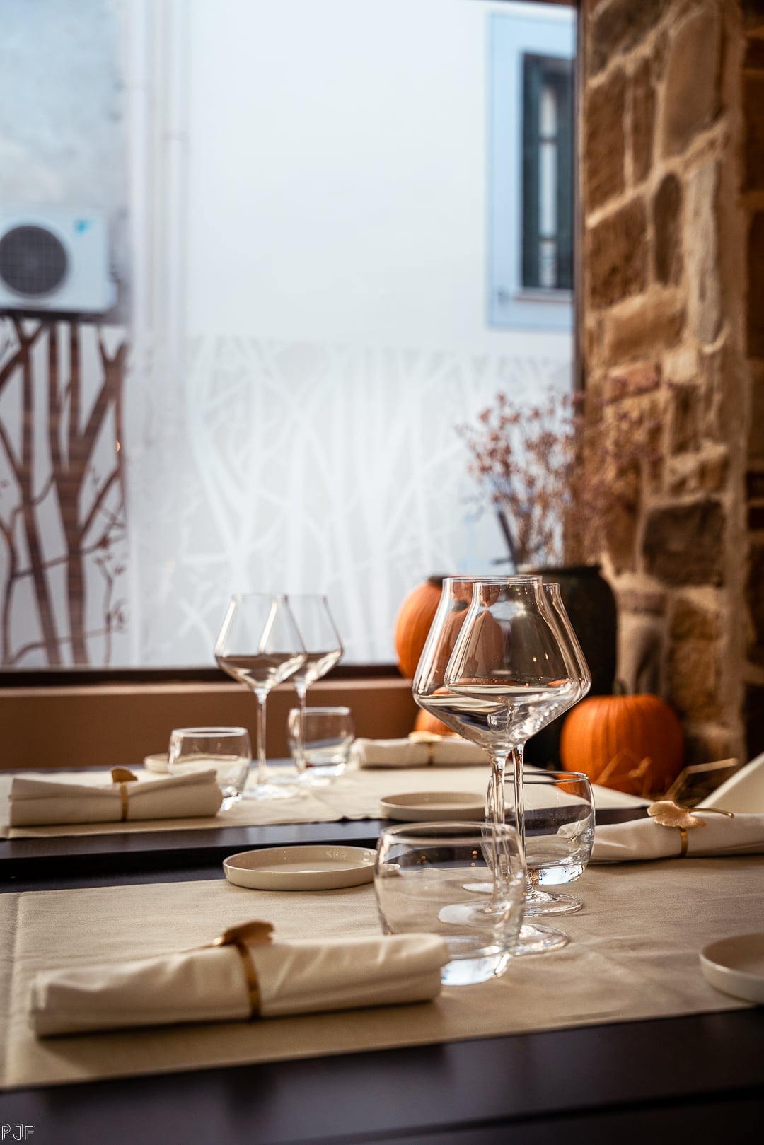 Le Petit Restaurant, Europe — Fine dining table set with wine glasses, cream linens, pumpkins, stone walls, and autumn light from arched windows.