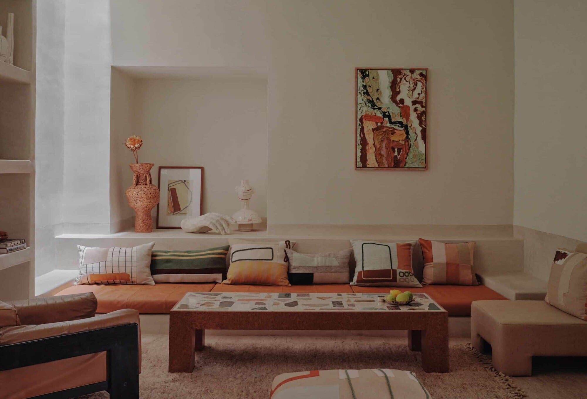 Rosemary, Africa — Sunlit living room with terracotta seating, layered cushions, geometric table, and ochre-toned walls creating warm minimalist hospitality interior.