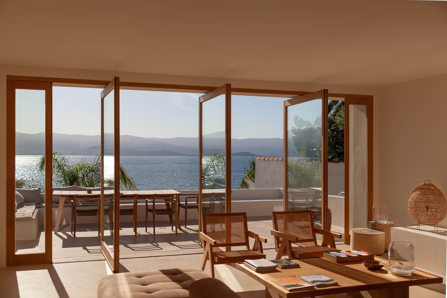 Casa Santa Teresa, Europe — Coastal villa interior with wooden pergola, rattan chairs, ocean views, and natural light streaming across terrazzo floors.
