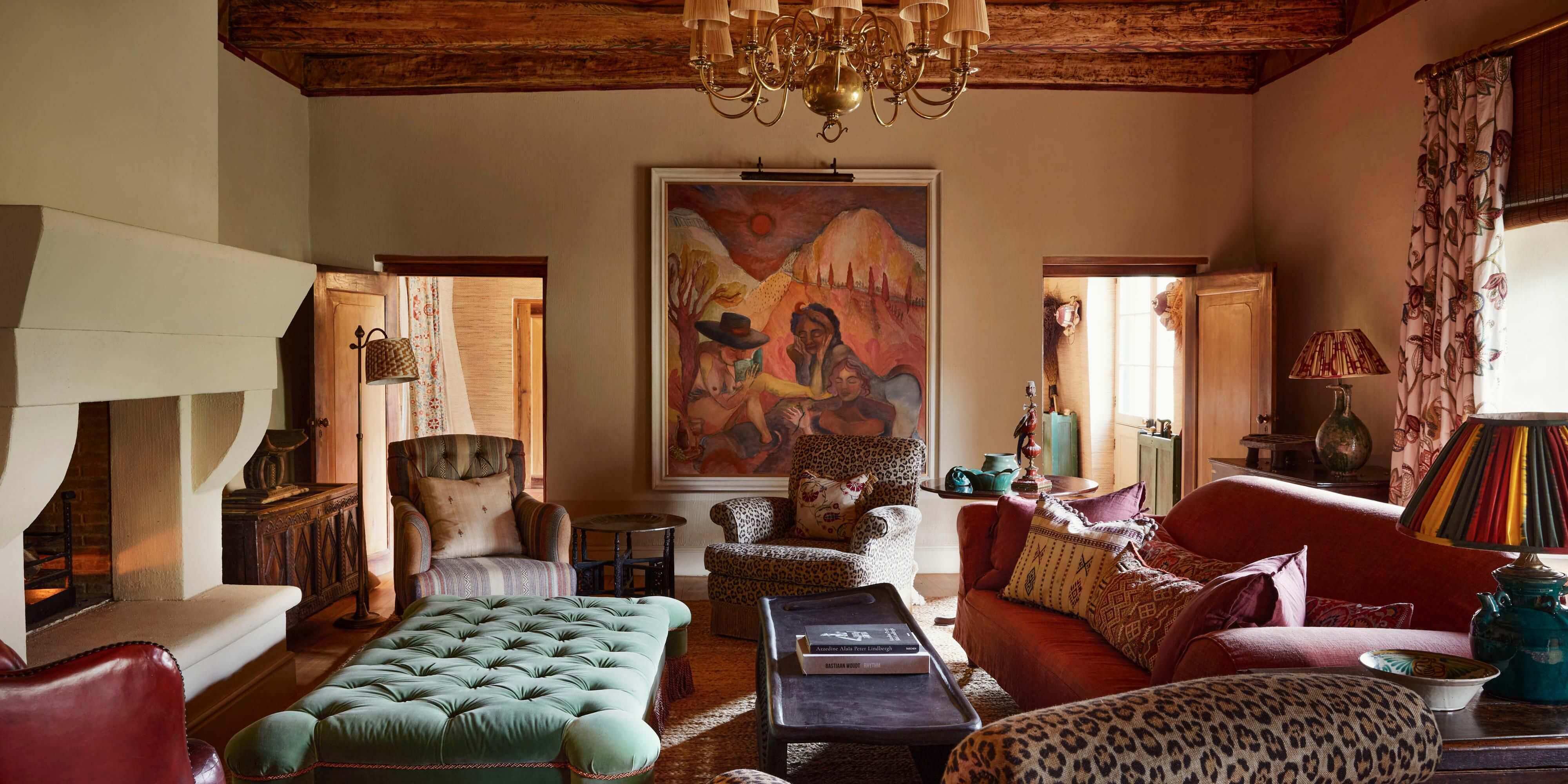Sterrekopje, Africa — Ochre-walled living room with exposed beam ceiling, leopard-print furnishings, tufted mint ottoman, and warm natural light streaming through tall windows.