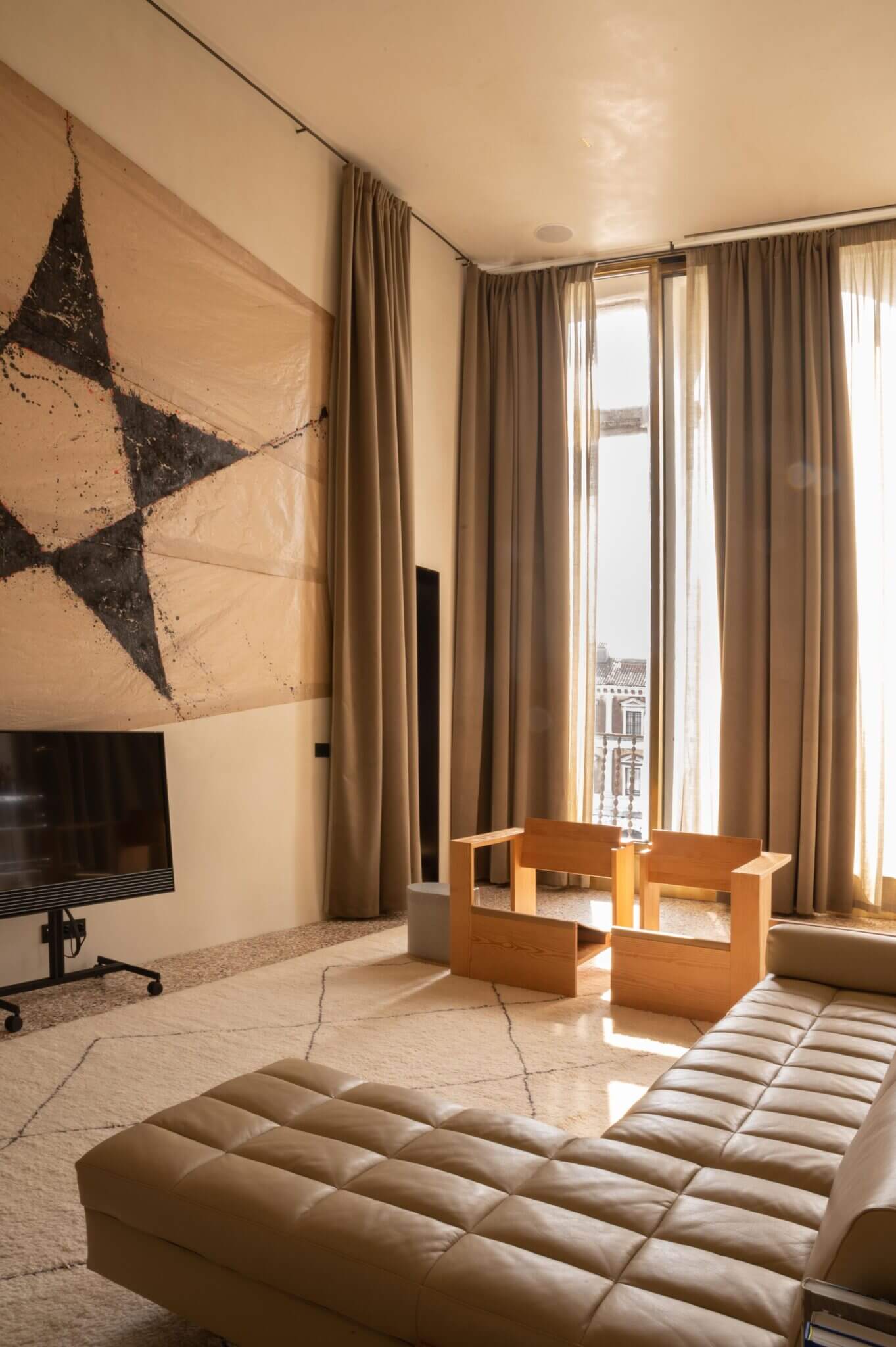 The Venice Venice Hotel, Venice, Europe — Minimalist luxury suite with geometric wall art, natural light through floor-to-ceiling windows, warm neutral palette, sculptural wooden furniture, quilted seating.