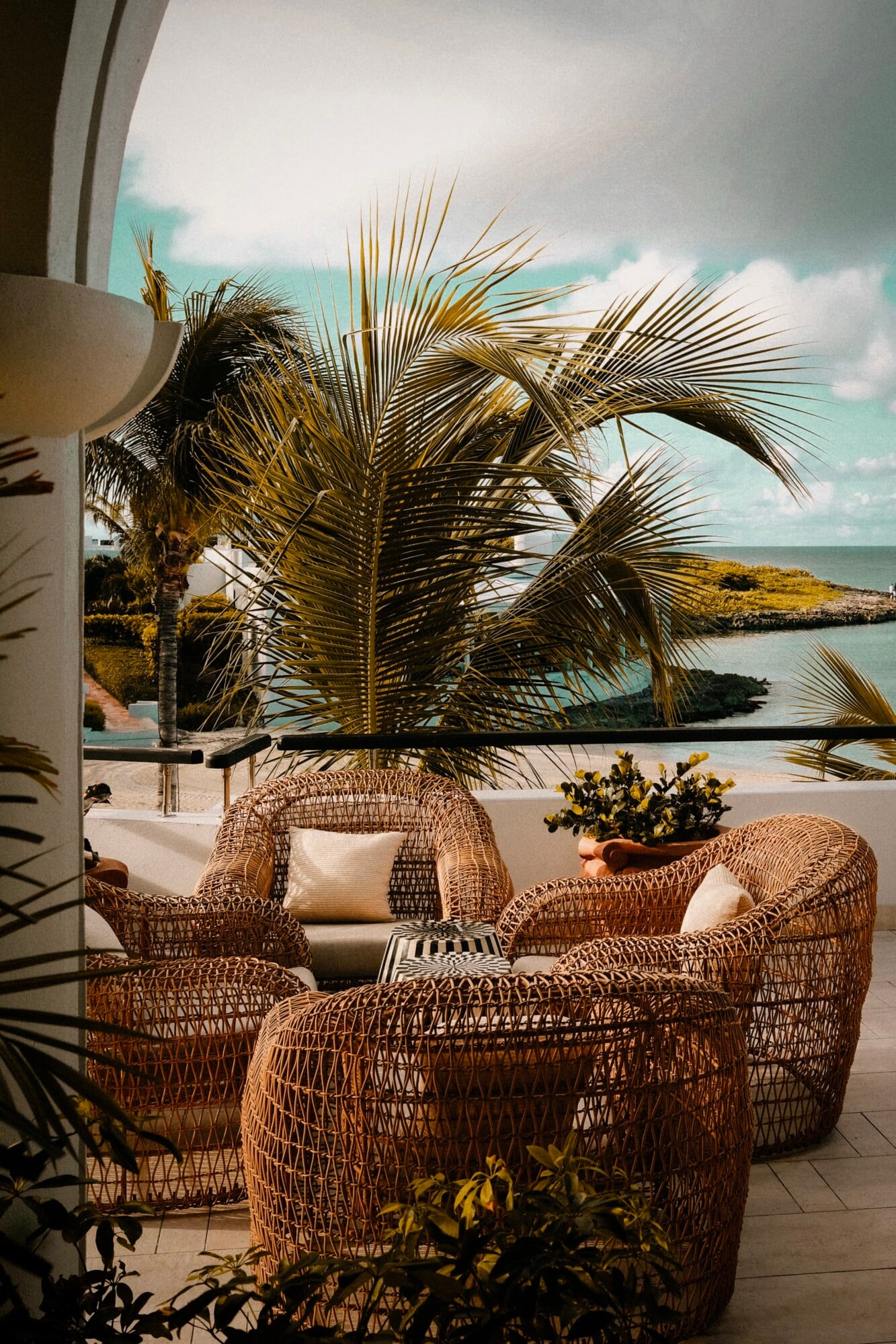 Cap Juluca, Anguilla — Woven rattan lounge chairs with ocean view terrace, palm fronds, and turquoise Caribbean waters at sunset.