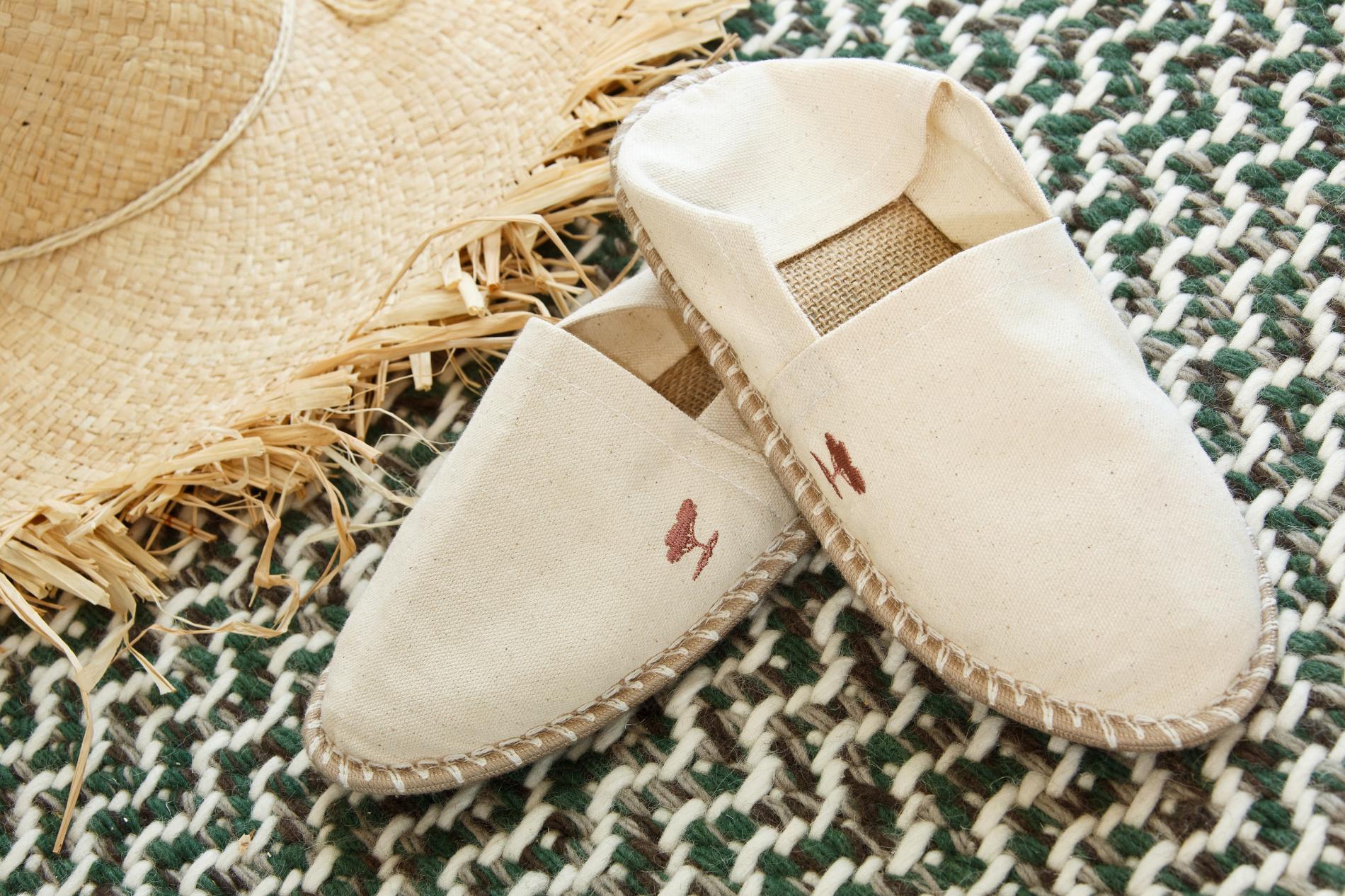 Hôtel Lou Pinet, Europe — Cream canvas slippers with embroidered detail beside woven straw hat on green and white textile, luxury hospitality styling.