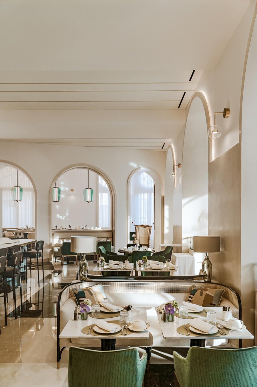 Carlton Cannes, Cannes, France — Elegant dining room with arched mirrors, marble tables, green velvet chairs, and natural light from tall windows.