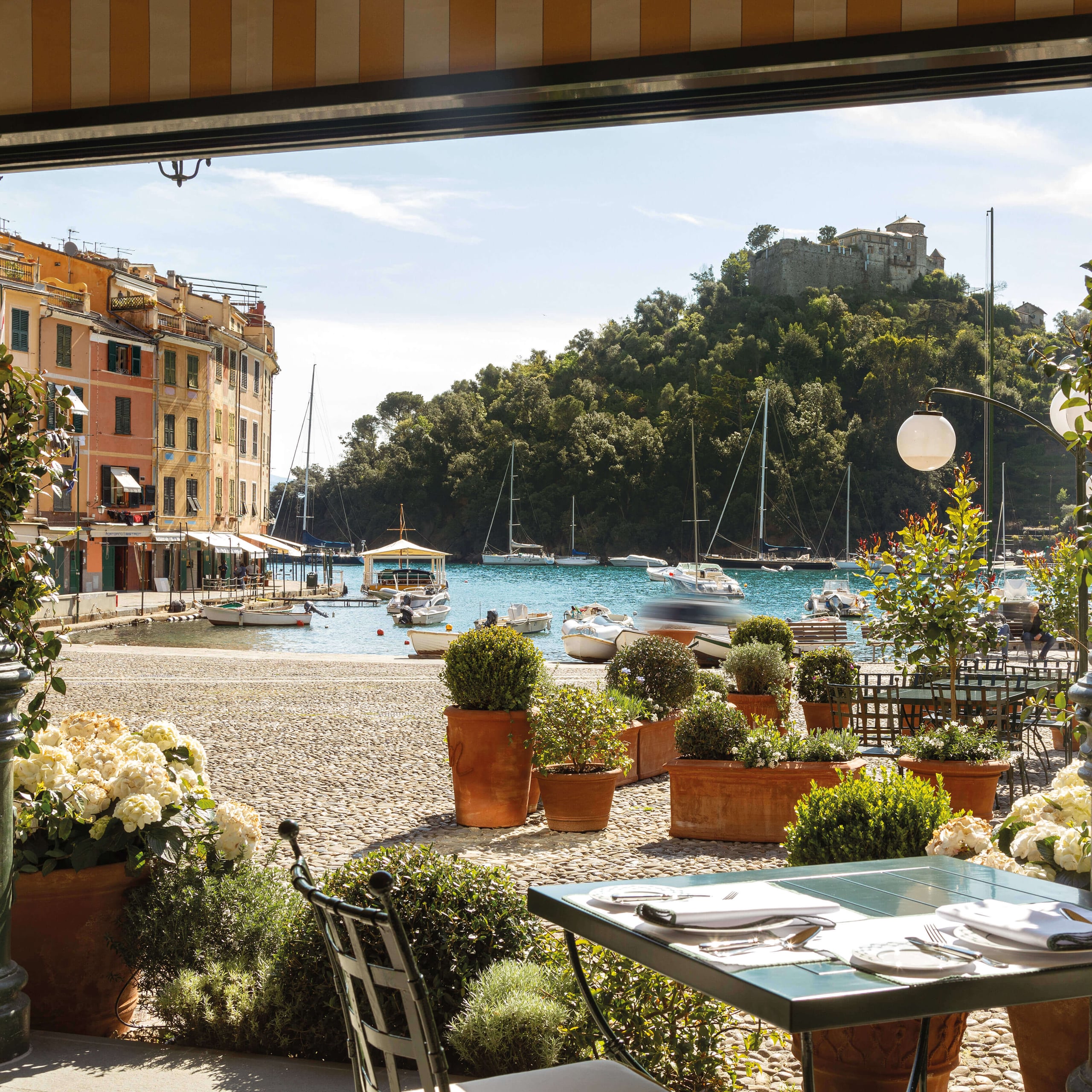 Splendido Mare, Europe — Waterfront terrace with sailboats, terracotta planters, and stone architecture overlooking Mediterranean bay at sunset.