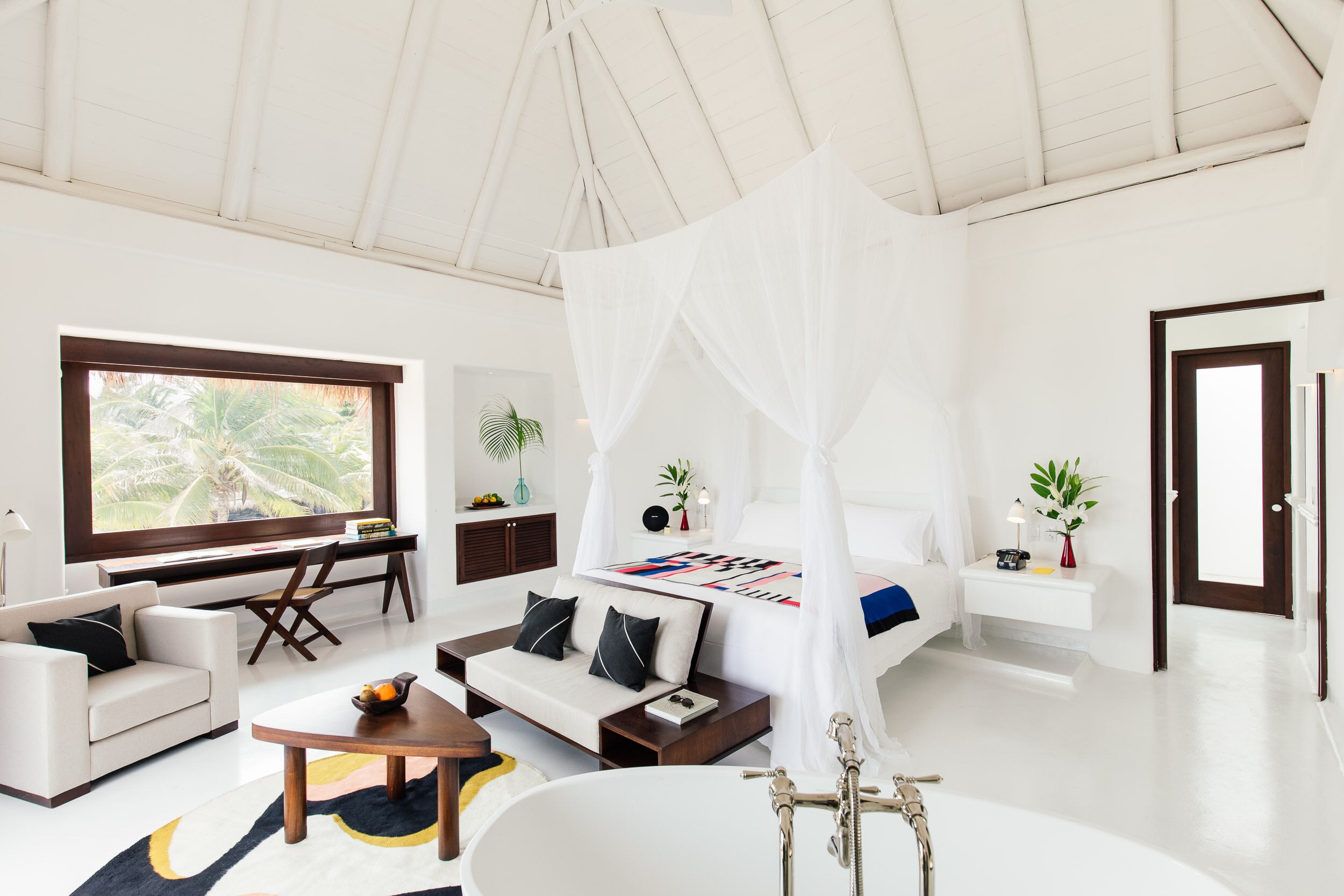 Hotel Esencia, Mexico — Minimalist oceanfront suite with vaulted ceiling, four-poster bed, dark wood accents, white linens, and panoramic palm views.
