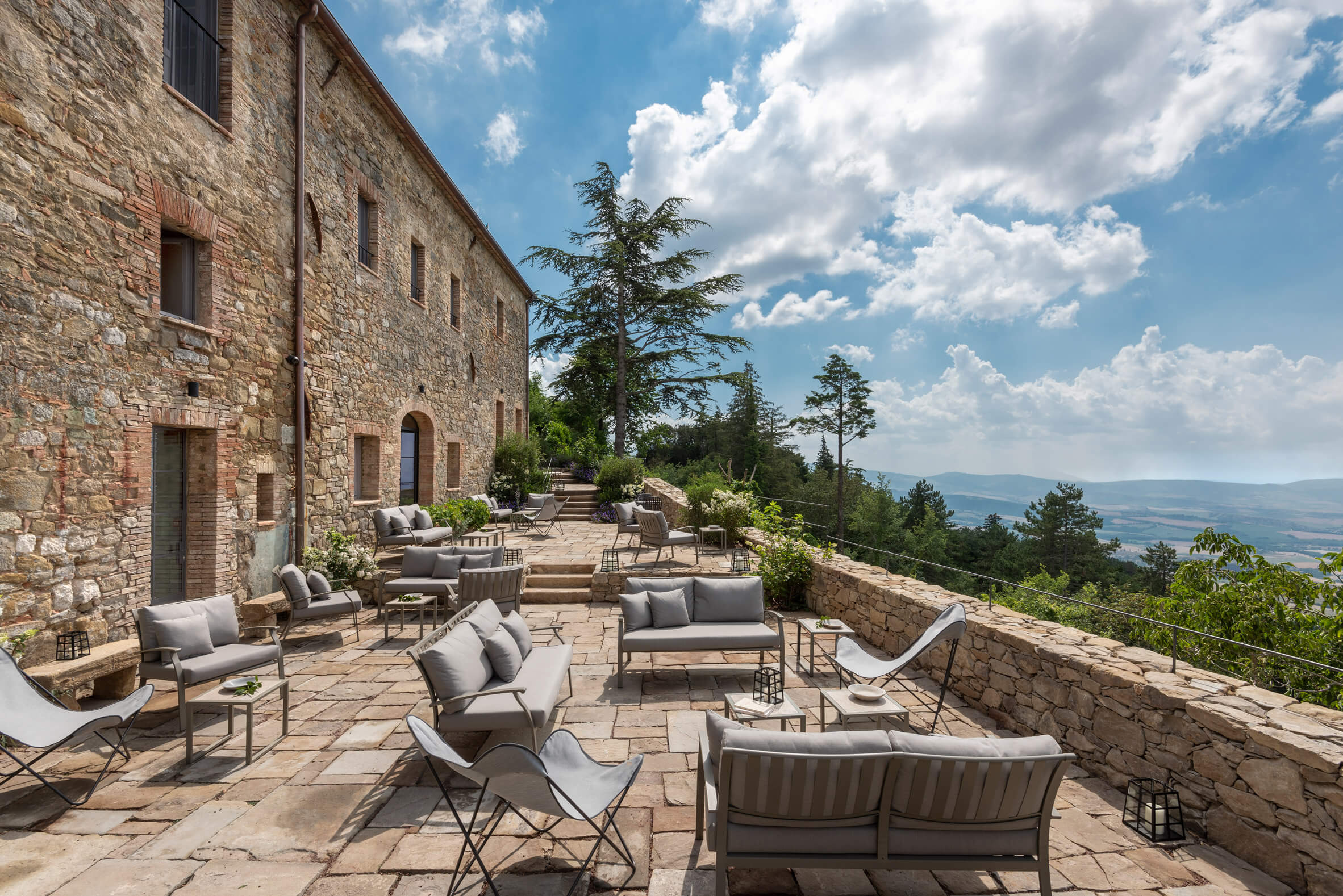 Stone terrace at Monteverdi with contemporary furnishings overlooking Tuscan countryside under bright skies.