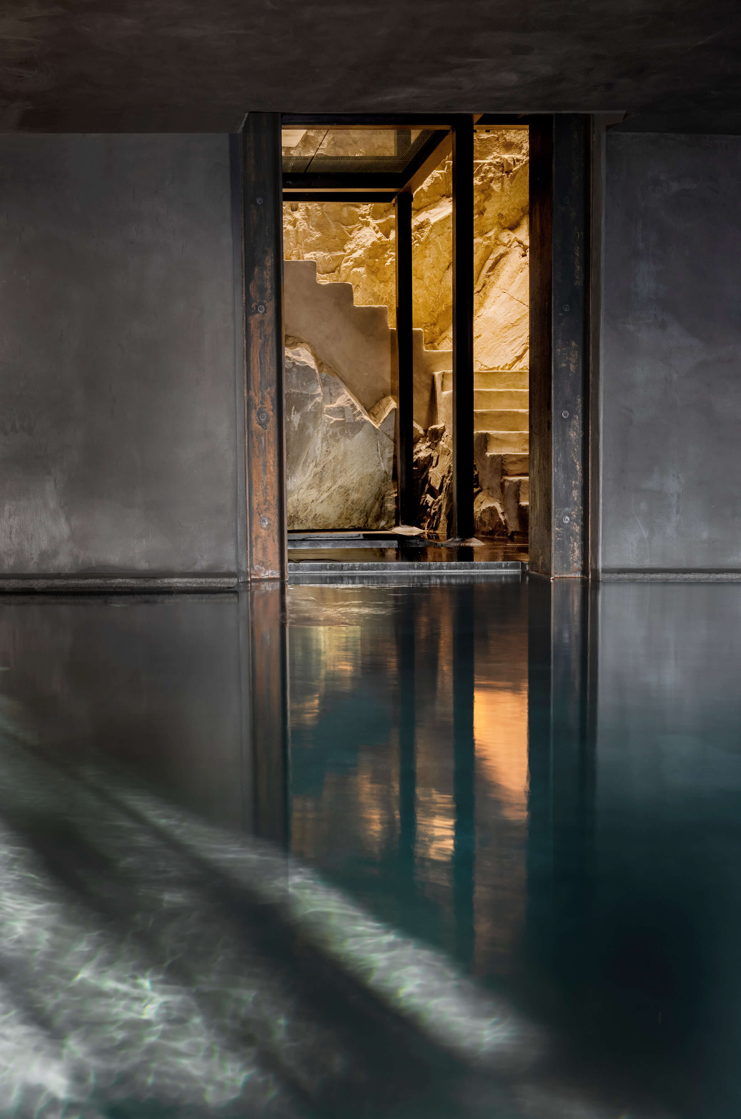 Monteverdi, Europe — Candlelit stone passageway with reflective water floor, warm golden light illuminating carved walls and stairs beyond dark doorframe.