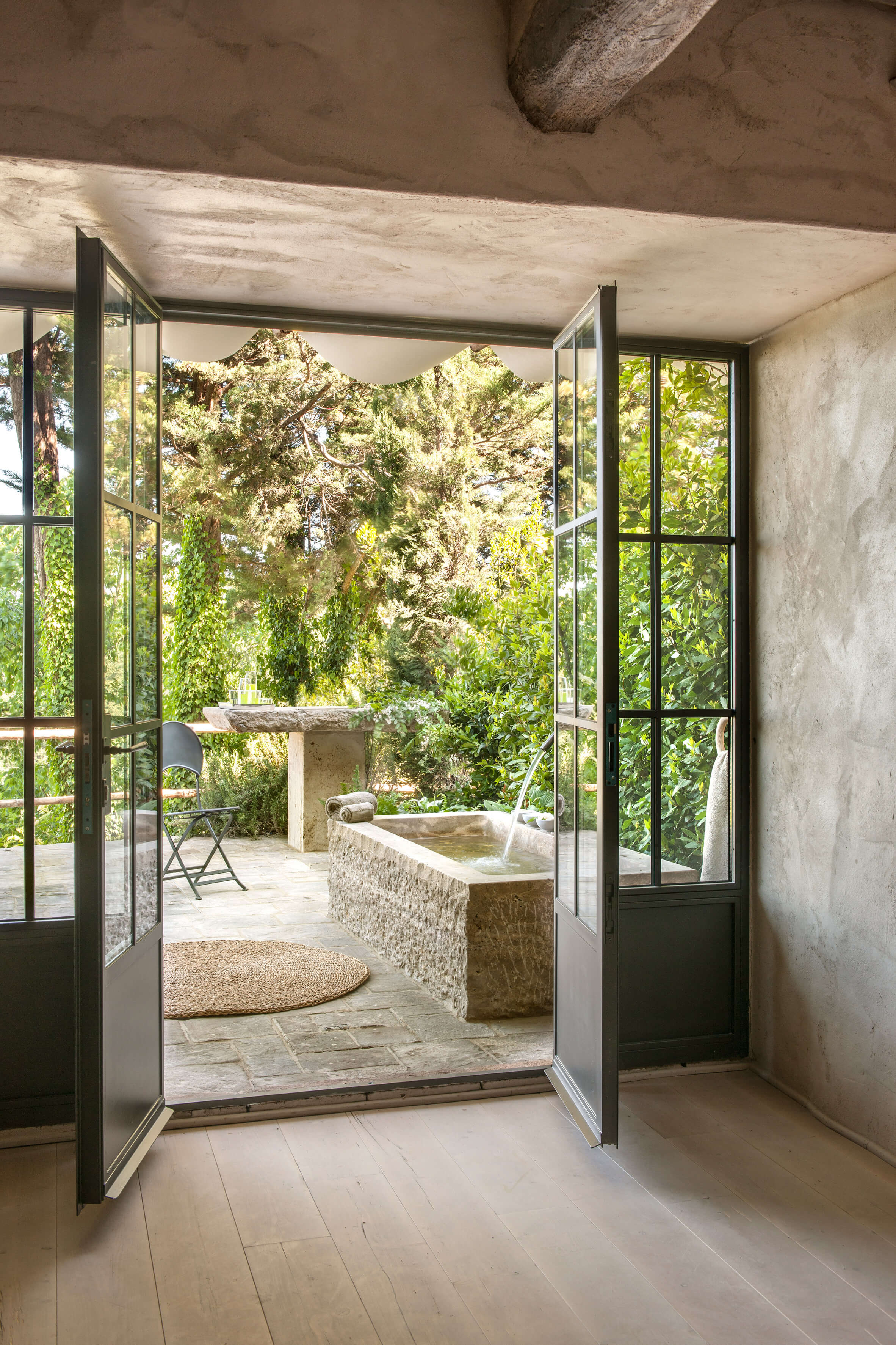 Monteverdi, Europe — Open steel-framed doors frame stone bathtub and garden beyond, concrete interiors with natural light and verdant landscape views.