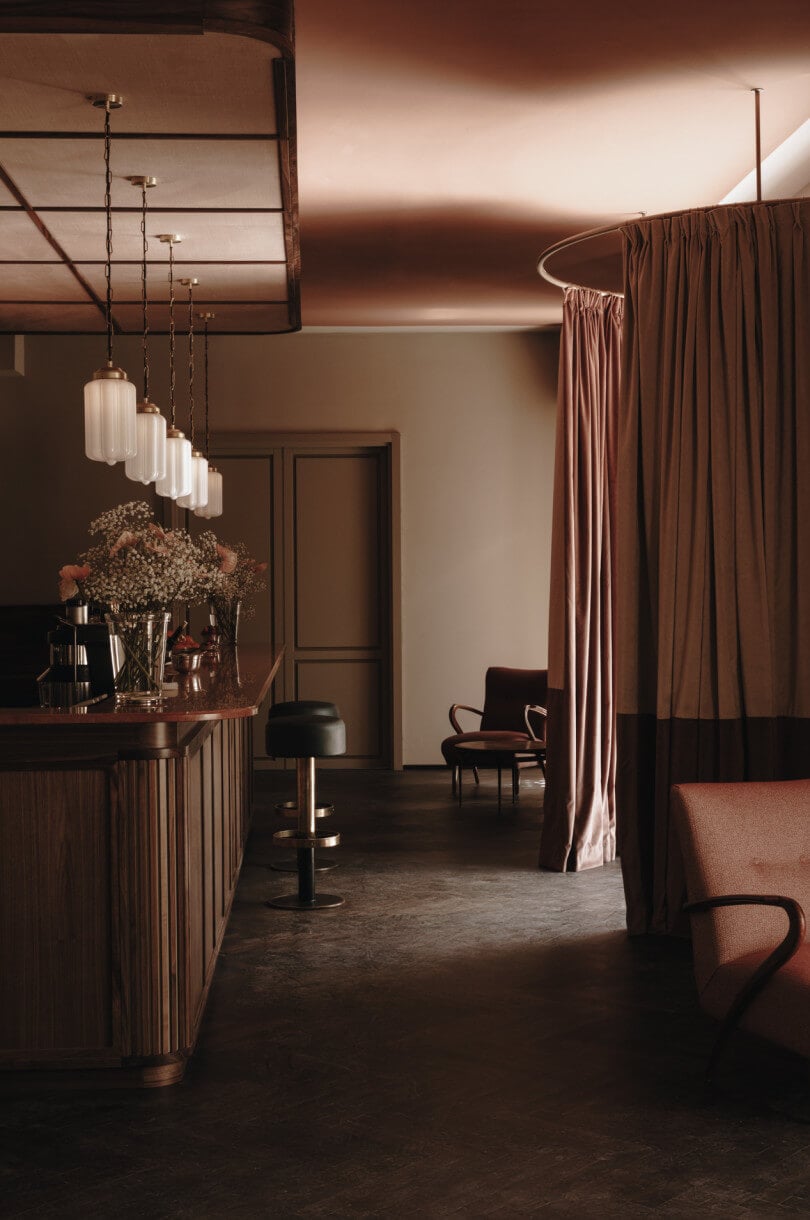 Parkhotel Mondschein, Europe — Warm-toned hospitality interior with pendant lights, wood paneling, terracotta curtains, and mid-century seating under ambient ceiling wash.