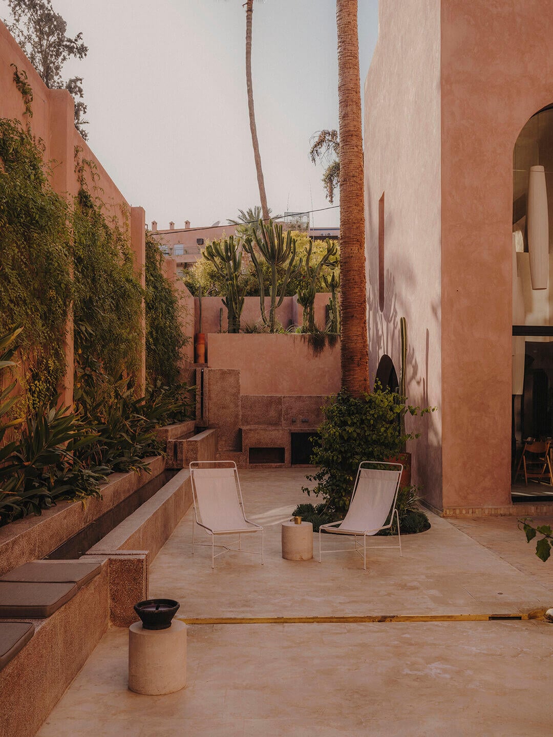 Maison Brummell Majorelle, Africa — Ochre courtyard with twin lounge chairs, tall palms, and terracotta walls under warm afternoon light.