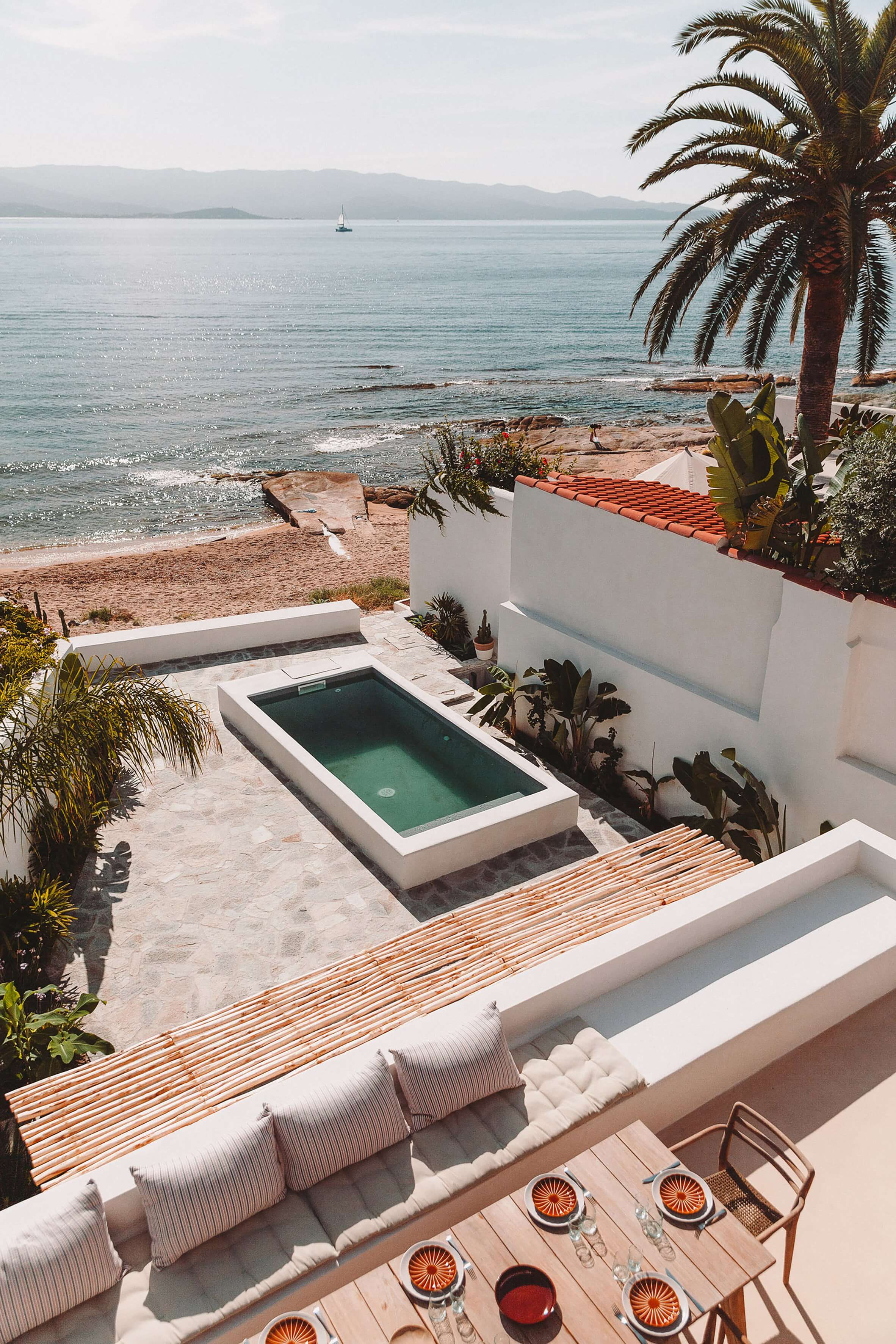 Casa Santa Teresa, Europe — Modernist clifftop villa with sunlit terrace, striped loungers, geometric pool, palm trees, and turquoise Mediterranean sea.