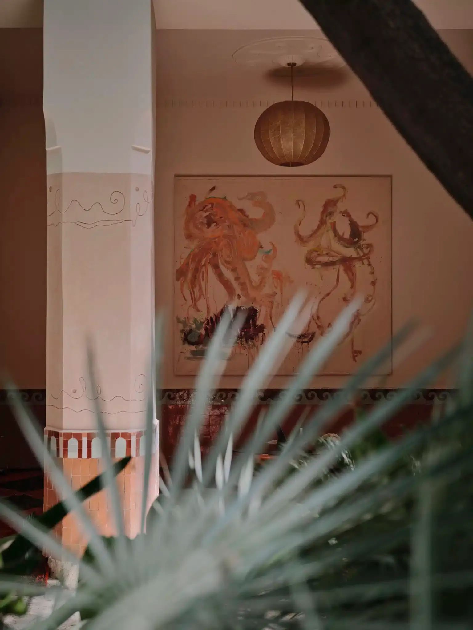 Rosemary, Africa — Terracotta wall mural with botanical pendant light and agave plant foreground, warm peach interior design detail.