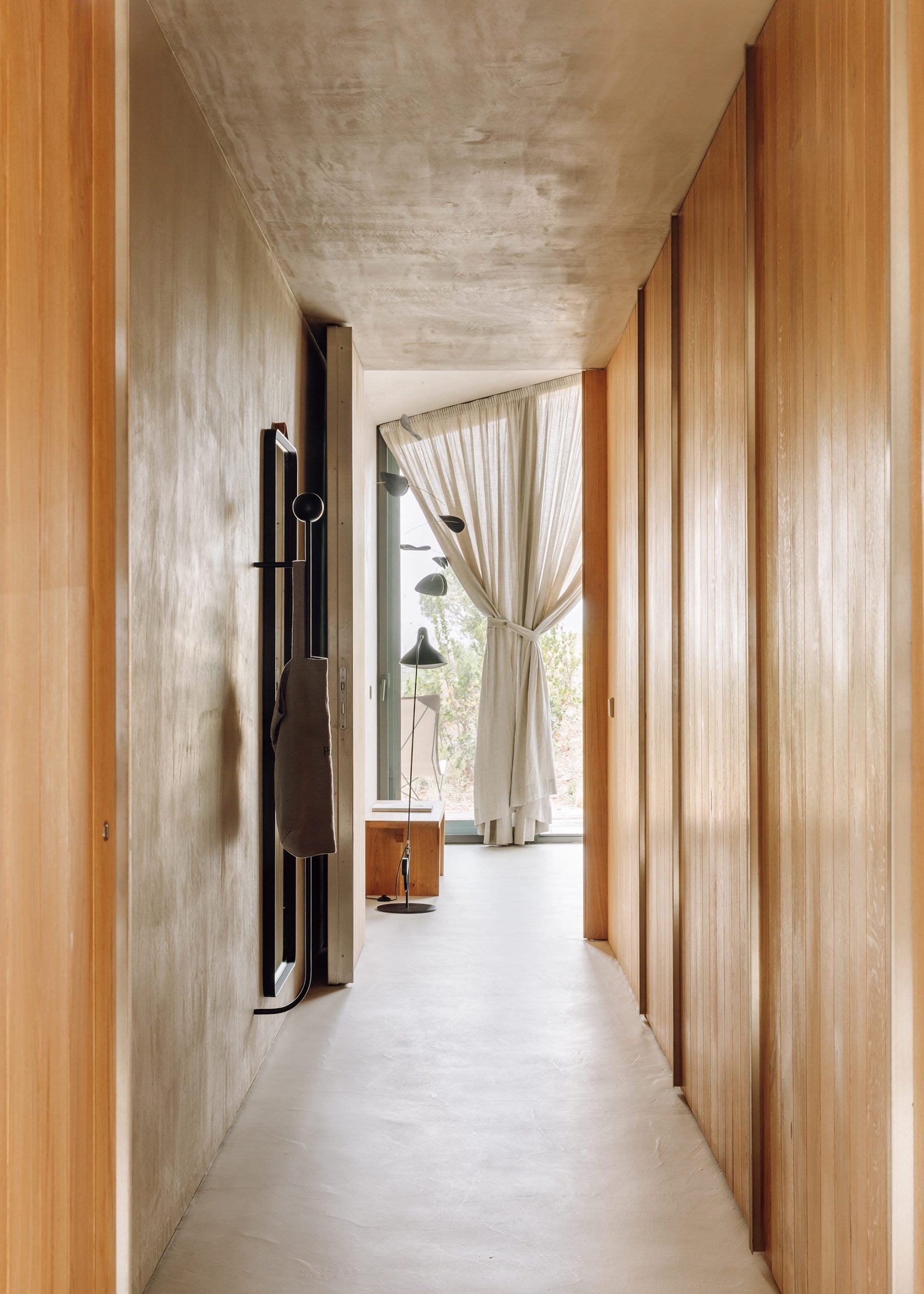 Pa.te.os, Europe — Concrete ceiling and timber-lined corridor with natural light, minimalist hallway leading to draped window and modern interior design.