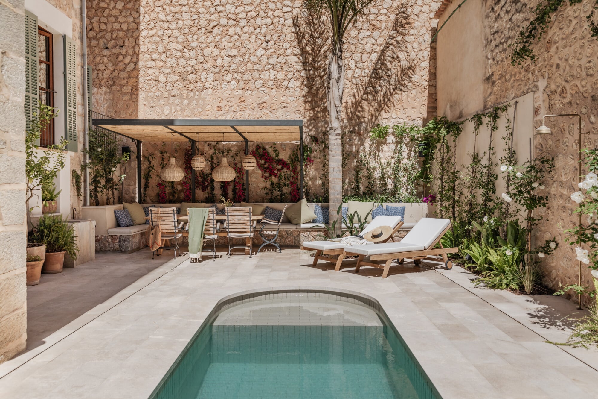 Mon Cor, Balearic Islands — Courtyard with narrow pool, pale stone walls, climbing ivy, lounge chairs, dining seating under pergola with hanging lanterns, Mediterranean architecture and design.