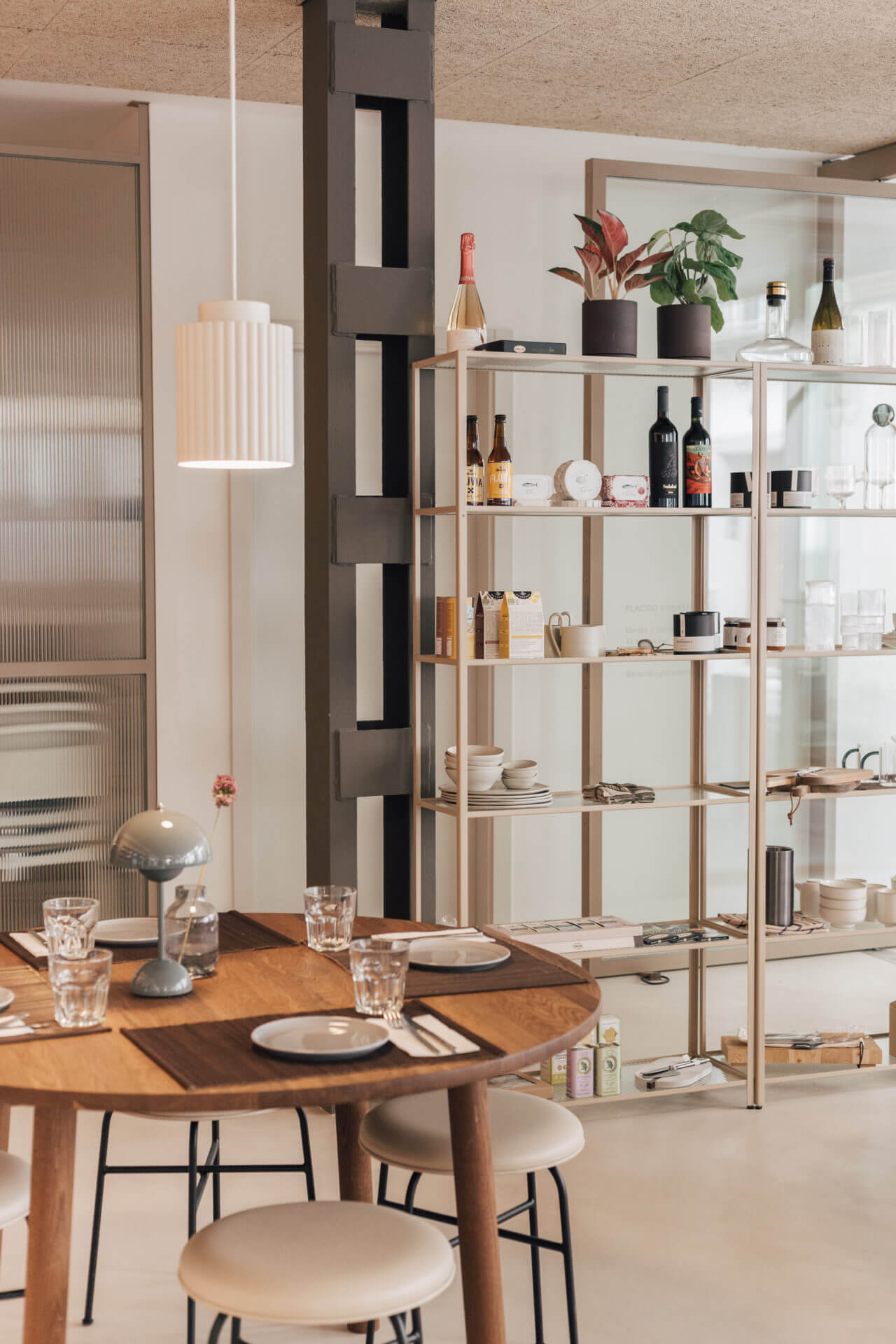 Plácido y Grata, Europe — Minimalist dining space with wooden round table, light oak shelving display, pendant lighting, and neutral interior design aesthetic.