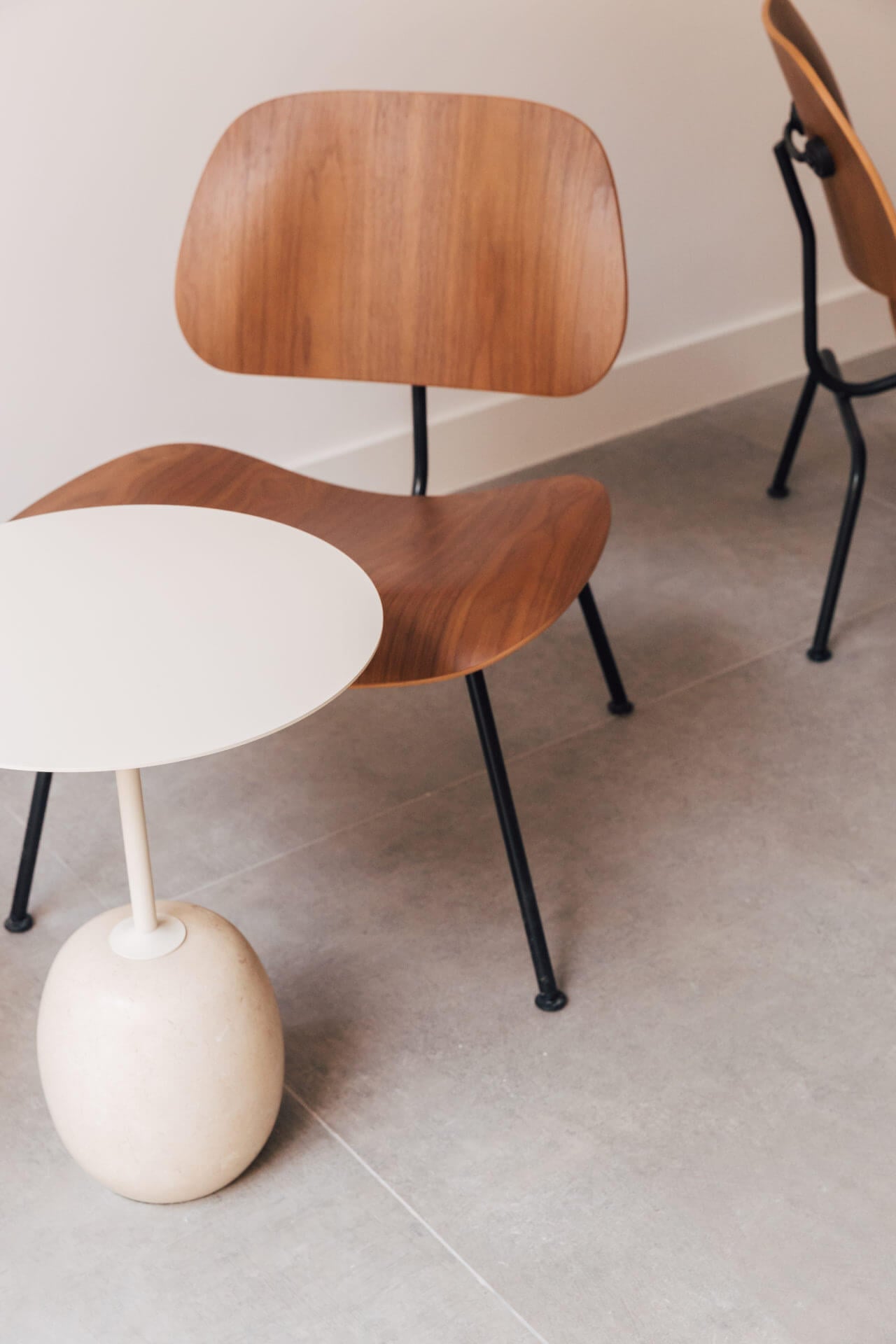 Plácido y Grata, Europe — Walnut chairs with curved plywood backs and black metal legs beside round white side table in minimalist hospitality interior.