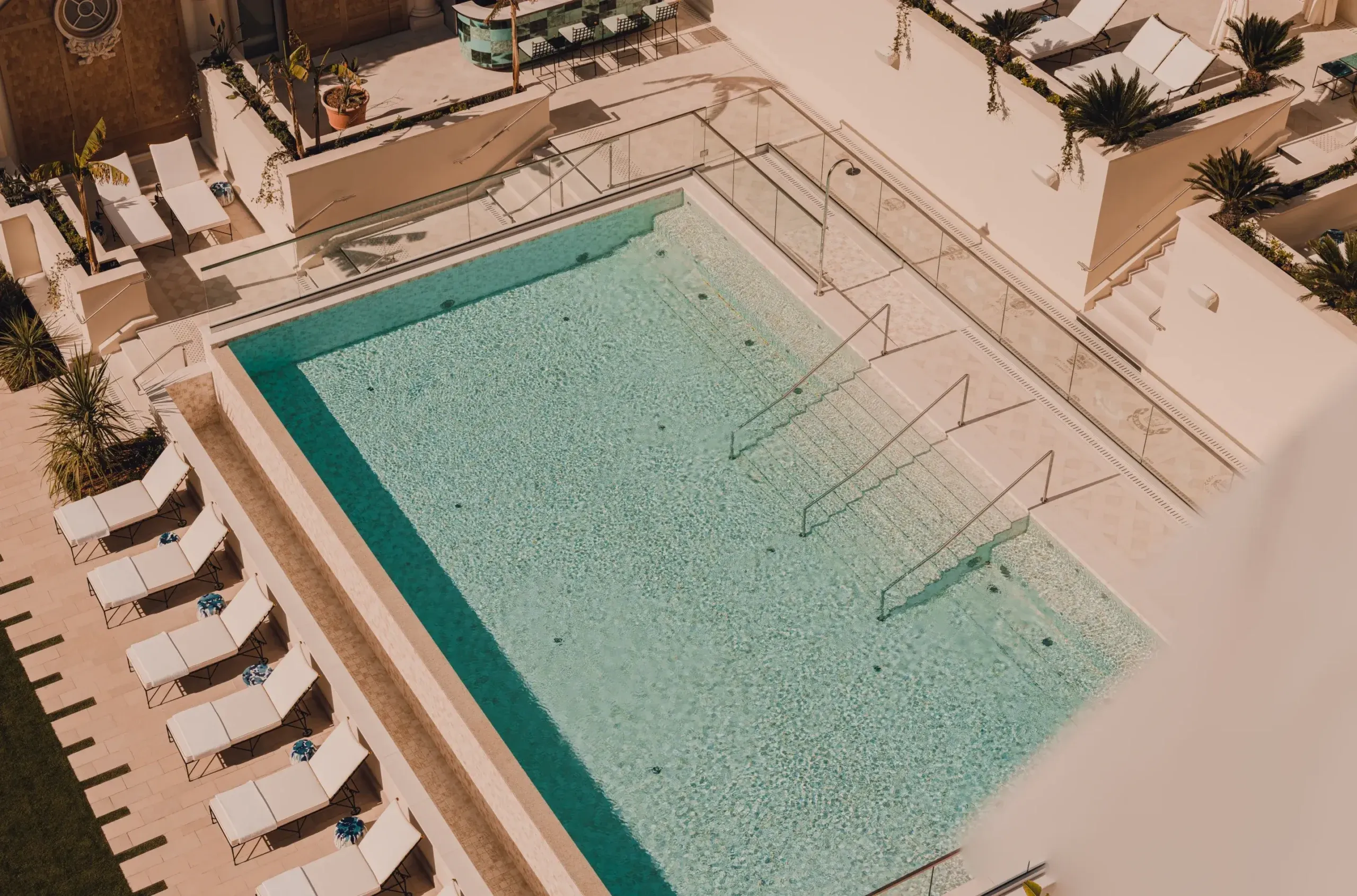 Carlton Cannes, Cannes, France — Aerial view of turquoise swimming pool with geometric lane dividers, cream loungers, and palm trees in Mediterranean resort courtyard.