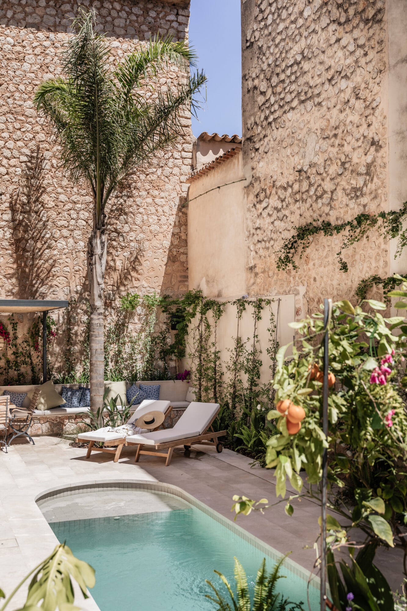 Mon Cor, Balearic Islands, Spain — Sunlit courtyard with pale stone walls, lounge chairs, climbing vines, and small pool surrounded by Mediterranean garden and historic architecture.