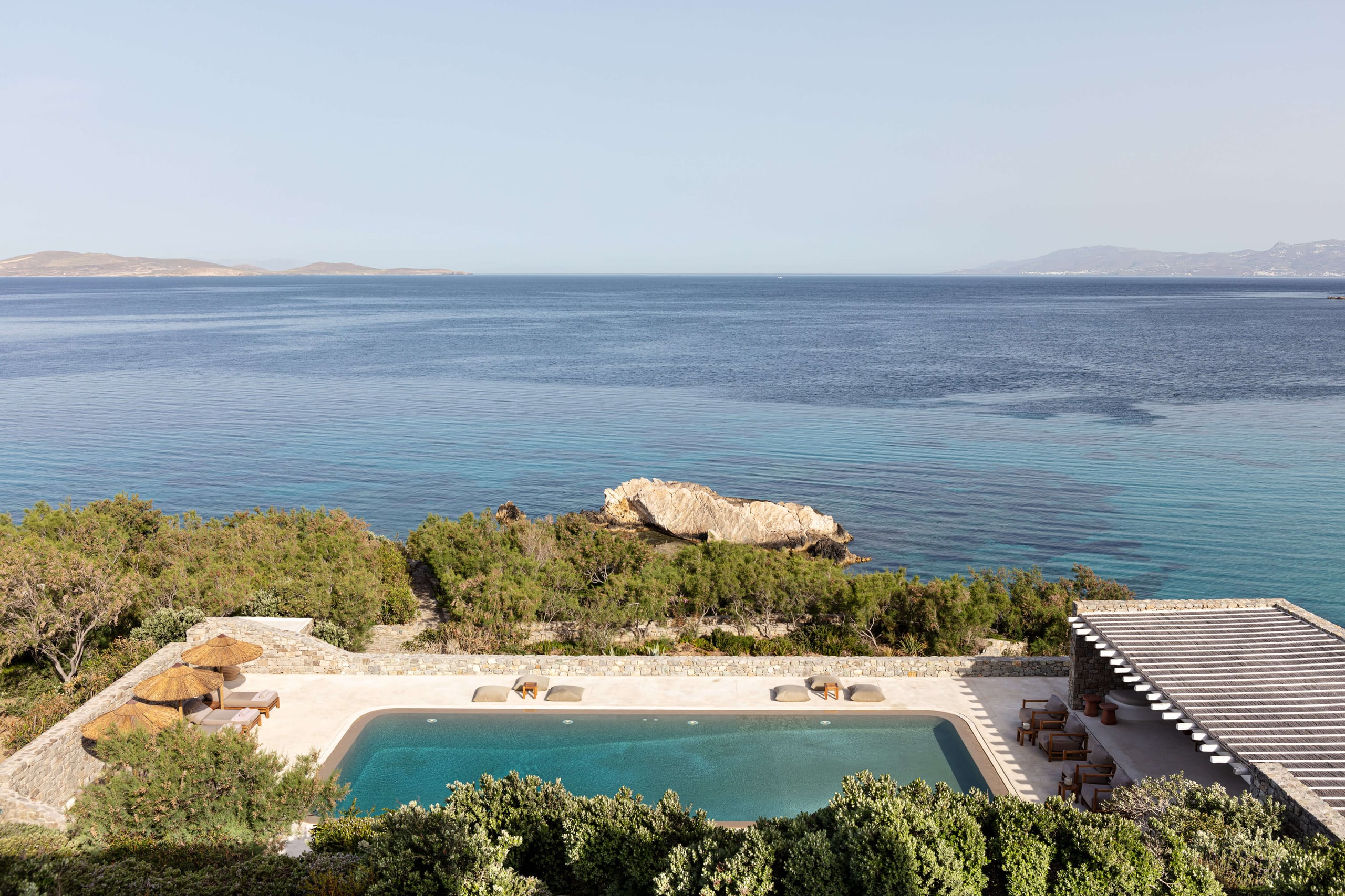 Villa Tama, Europe — Modernist clifftop villa with turquoise pool overlooking Aegean Sea, terraced limestone architecture and Mediterranean vegetation.