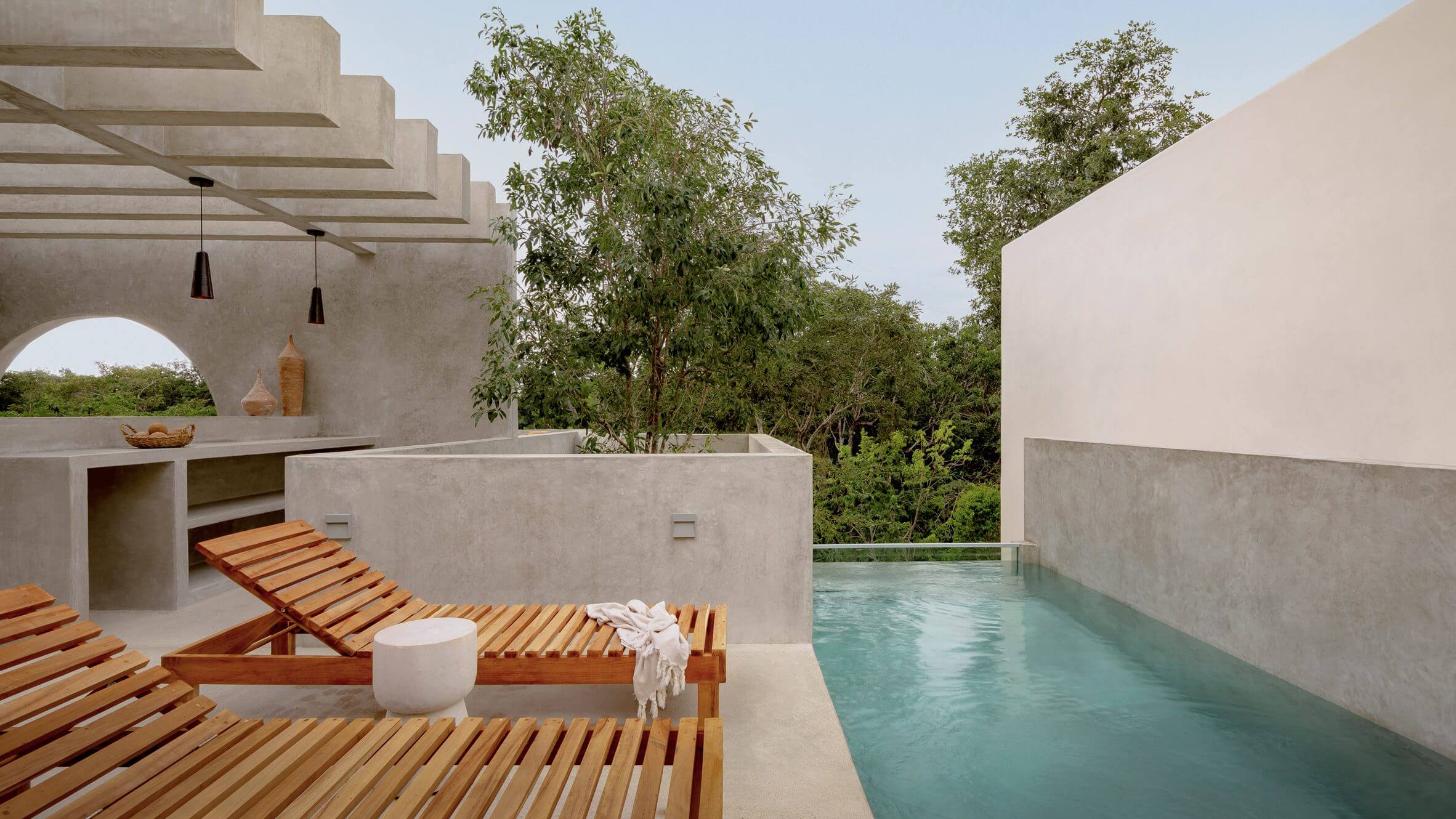 Villa Cava, Mexico — Modernist concrete pavilion with infinity pool, wooden lounge chairs, and native tree canopy framing minimalist outdoor living space.