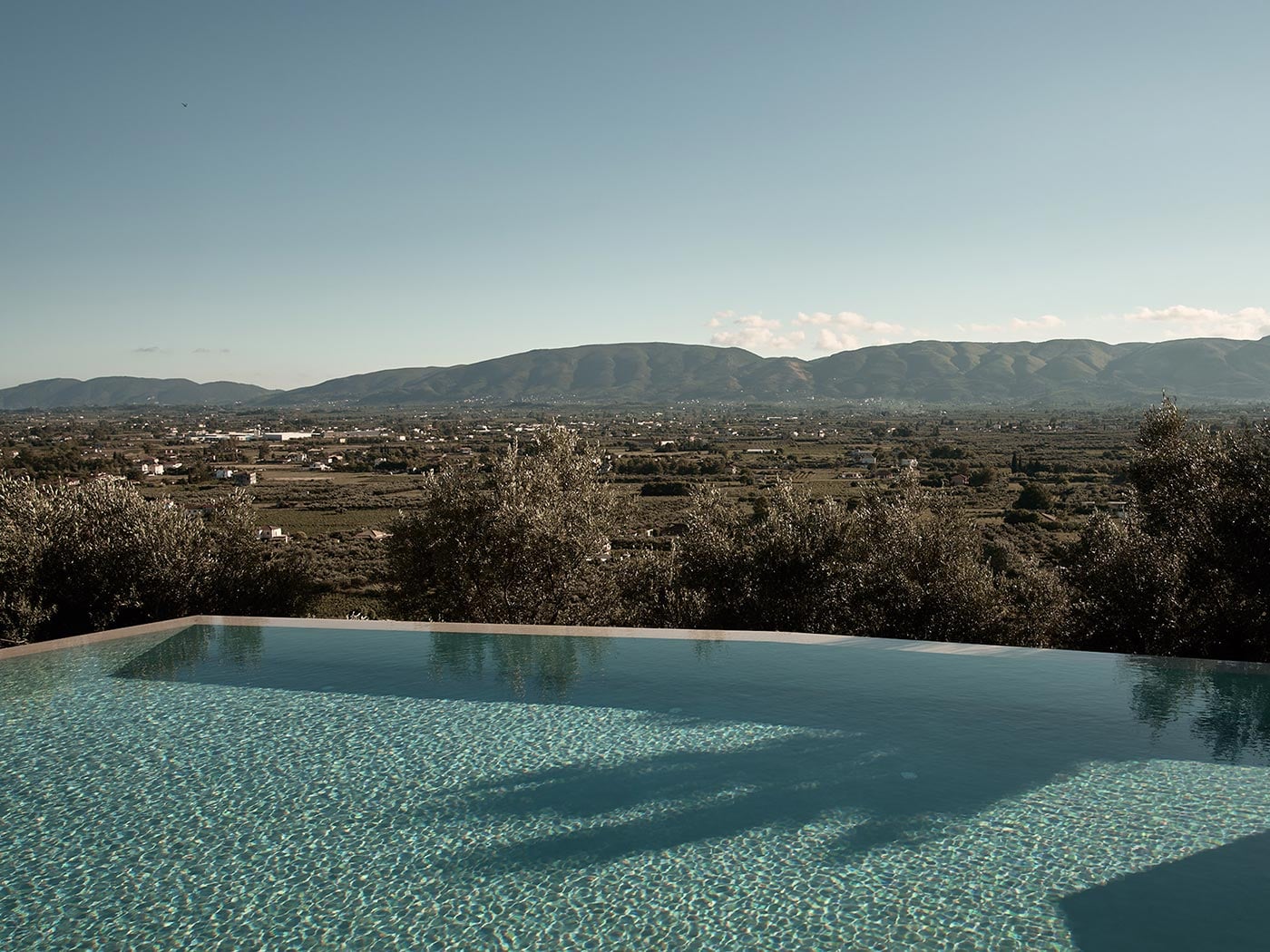 Olea All Suite Hotel, Europe — Infinity pool with turquoise water overlooking olive groves and mountain valley landscape at golden hour.