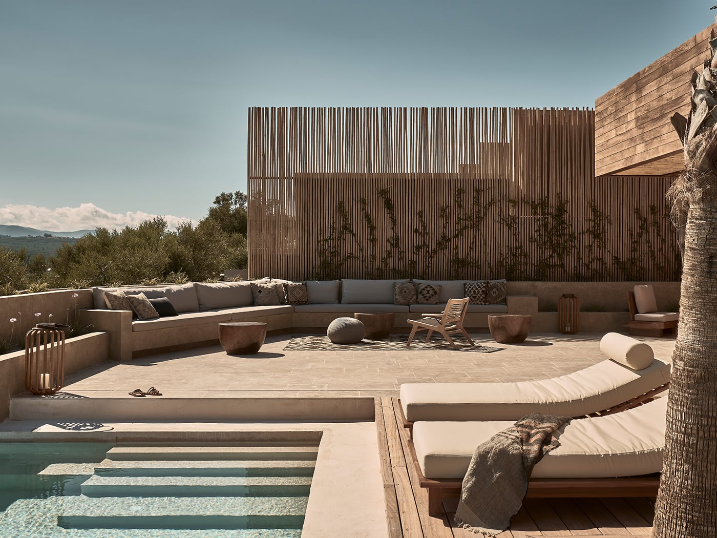 Olea All Suite Hotel, Europe — Minimalist poolside terrace with curved loungers, built-in seating, wooden privacy screen, and mountain views under clear sky.