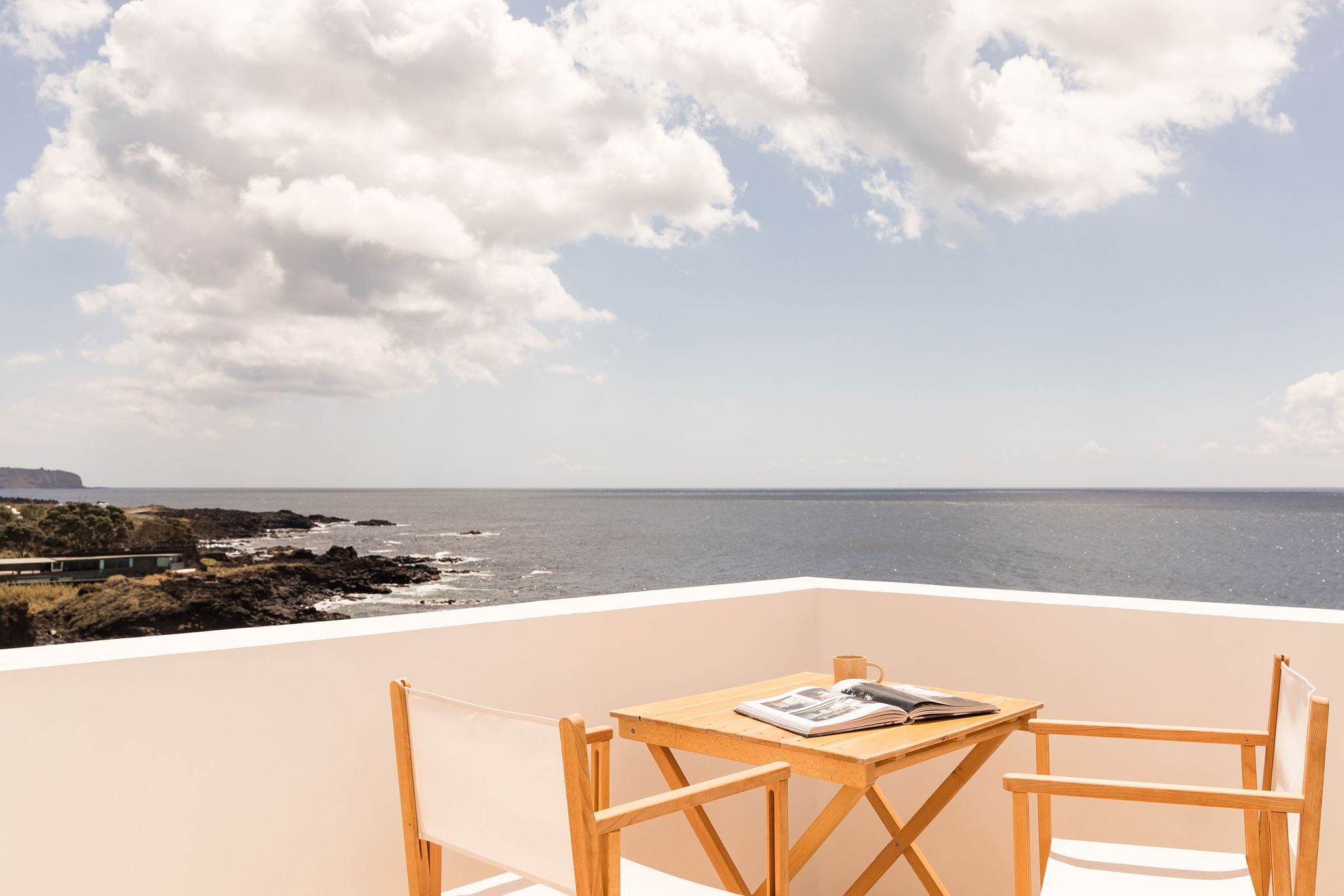 White Hotel, Europe — Minimalist wooden furniture on expansive terrace with sea view, natural light, coastal landscape, luxury hospitality design.