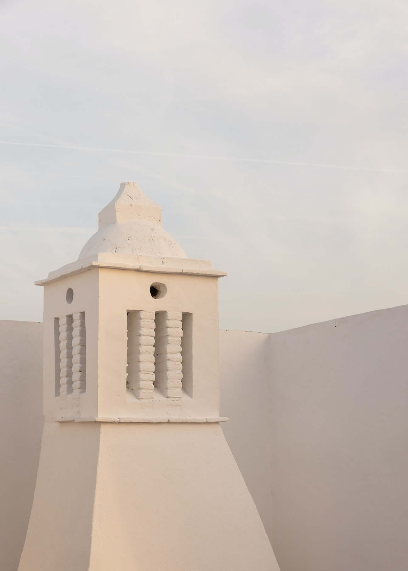 Casa Quatro, Europe — Whitewashed chimney tower with geometric vents and tapered roof against minimal sky, architectural detail of Mediterranean villa.