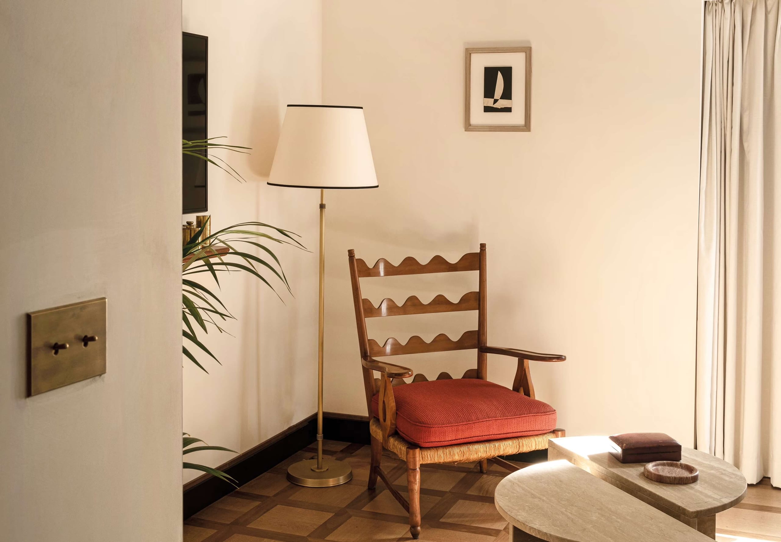Splendido Mare, Europe — Modernist sitting room with ladder-back chair, coral cushion, brass floor lamp, pale walls, and geometric parquet flooring.